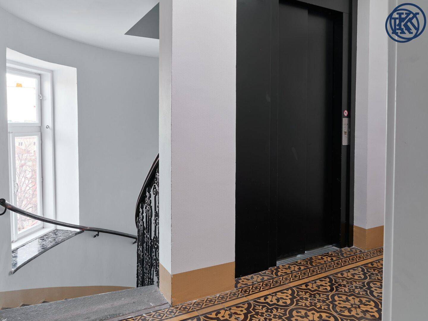 Treppenhaus mit schmiedeeisernem Geländer und einem modernen Aufzug.