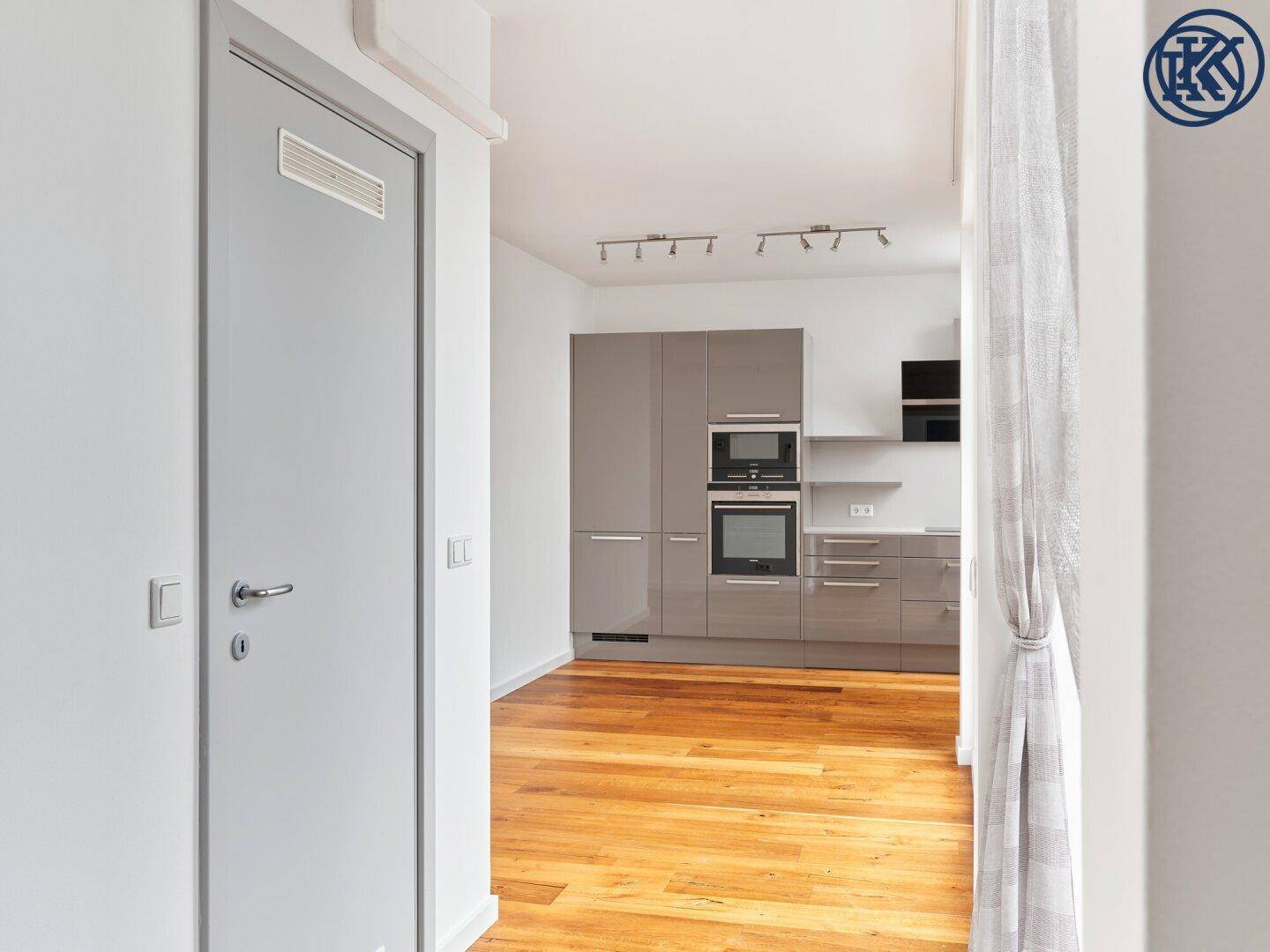 Blick vom Flur in eine moderne Küche mit grauen Schränken und Holzboden.