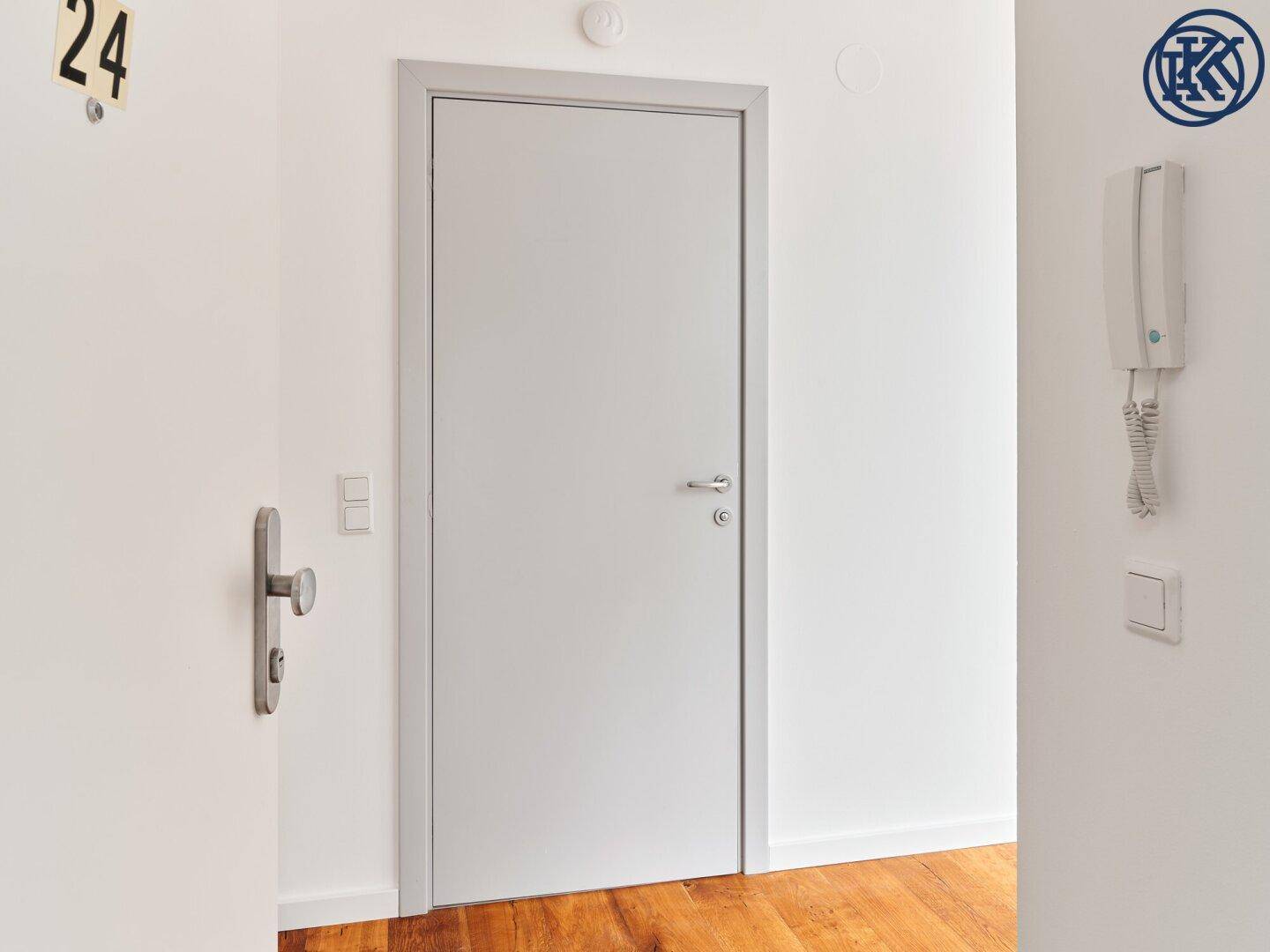 Heller Flur mit weißer Tür, Gegensprechanlage und Holzboden im Eingangsbereich der Wohnung.