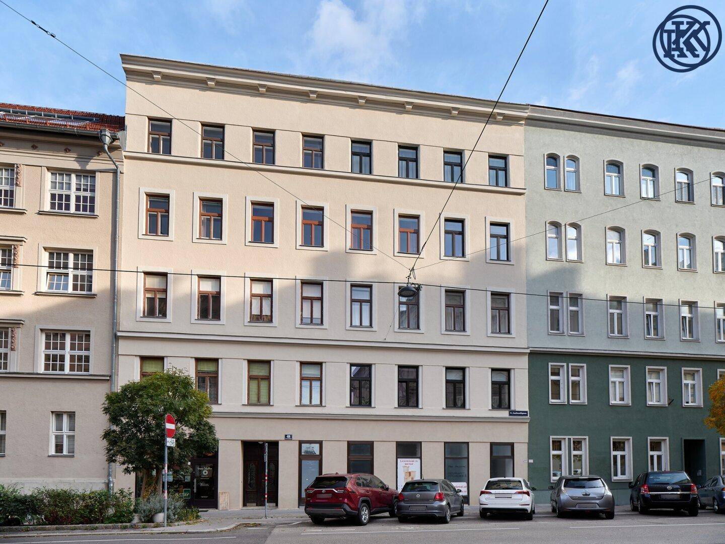 Ansicht eines gepflegten Wohngebäudes mit heller Fassade und traditionellen Fenstern in urbaner Umgebung.