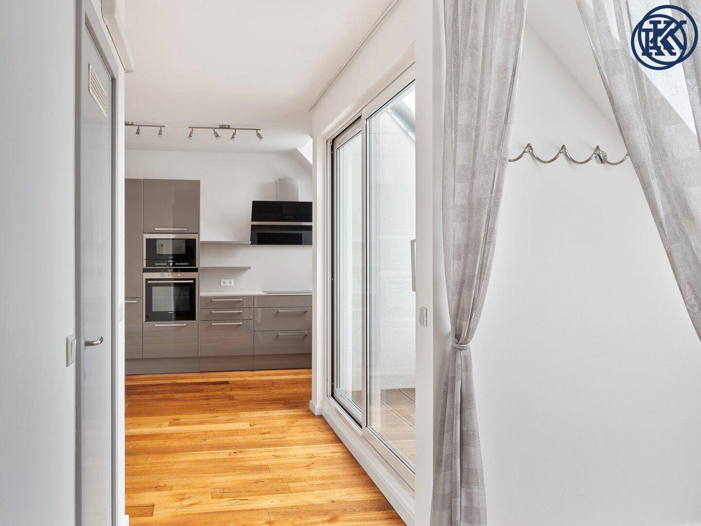 Heller Flur mit Holzboden, der zu einer modernen Küche und einem Balkon führt.