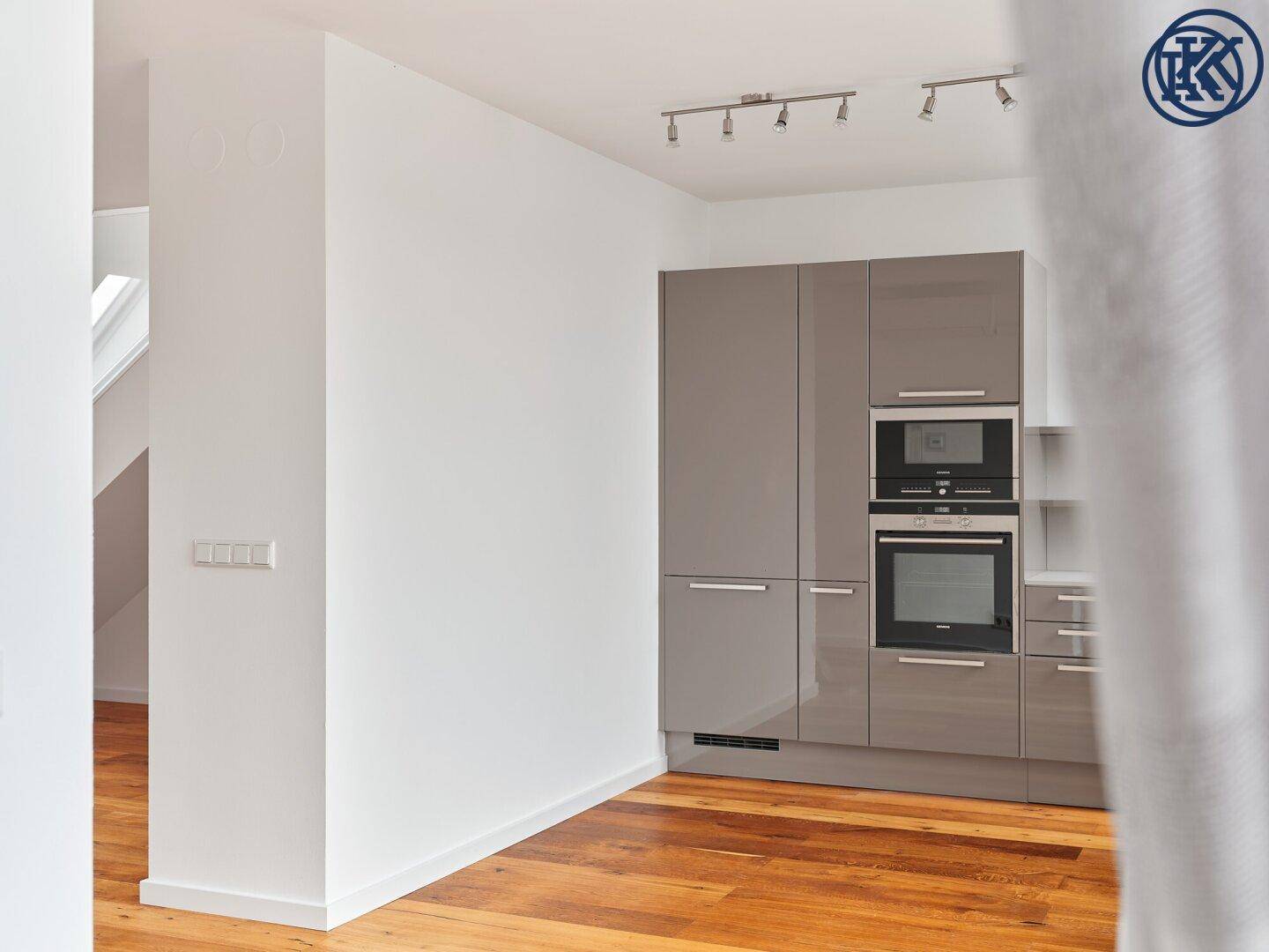Moderne Küche mit grauen Hochglanzschränken, integrierten Geräten und Holzboden.