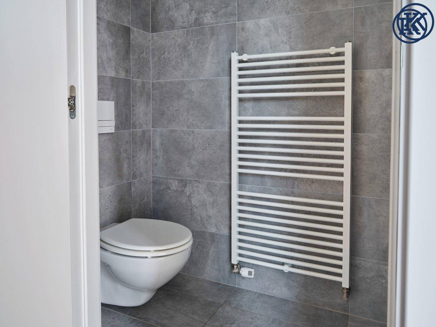 Modernes Gäste-WC mit grauen Fliesen, wandhängendem WC und beheiztem Handtuchhalter.