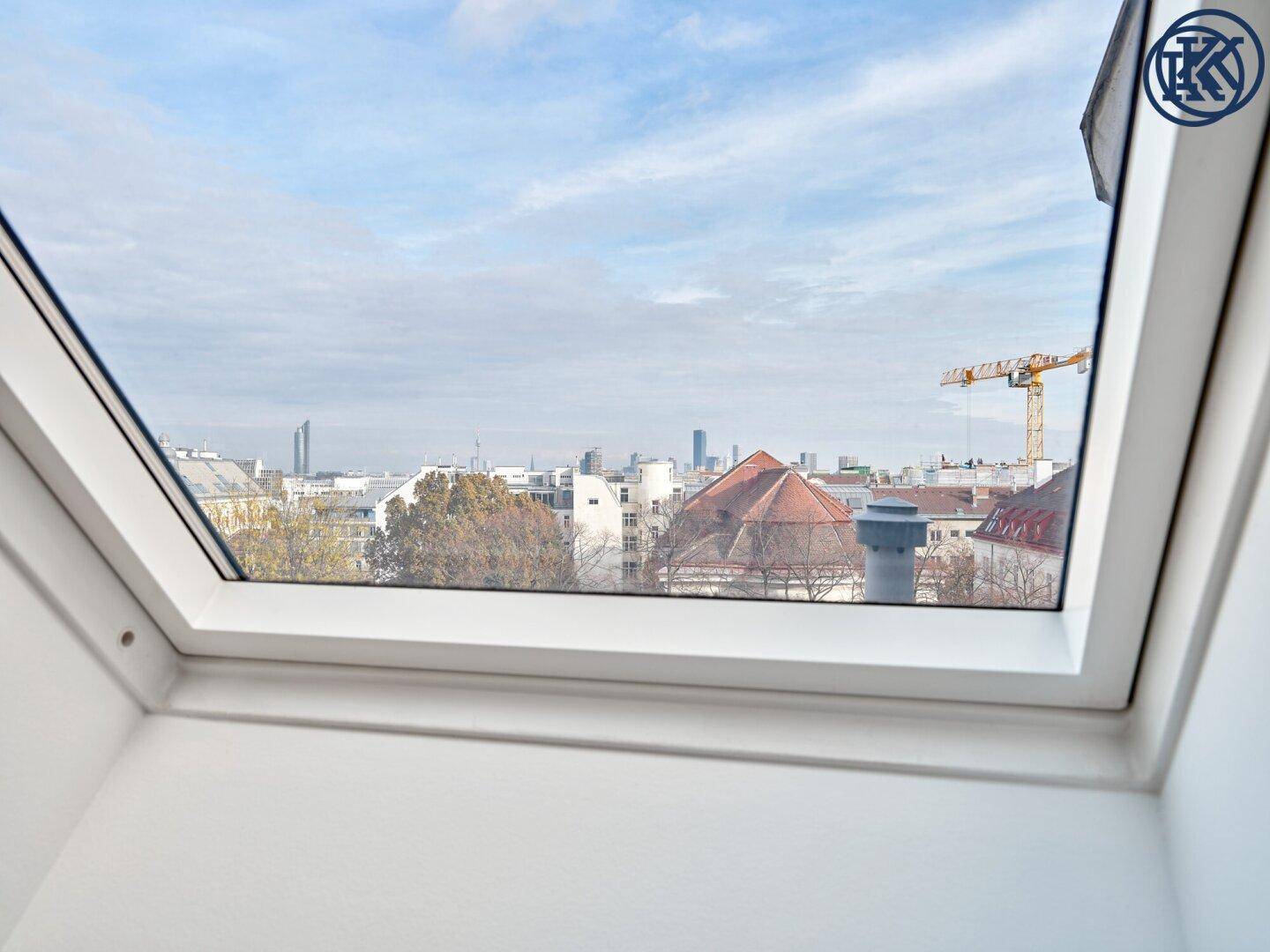 Ausblick aus einem Dachfenster auf die Stadtlandschaft mit Gebäuden und einem Kran.