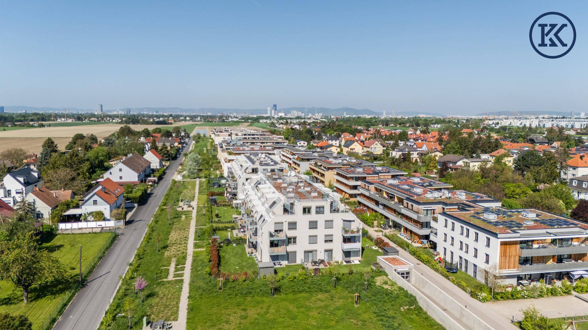 Panoramablick auf eine moderne Wohnsiedlung mit weiten Grünflächen und Stadtsilhouette am Horizont.