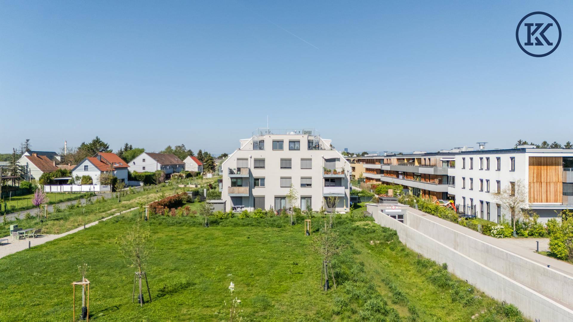 Weitläufige Grünfläche vor modernen Wohngebäuden unter klarem blauem Himmel.