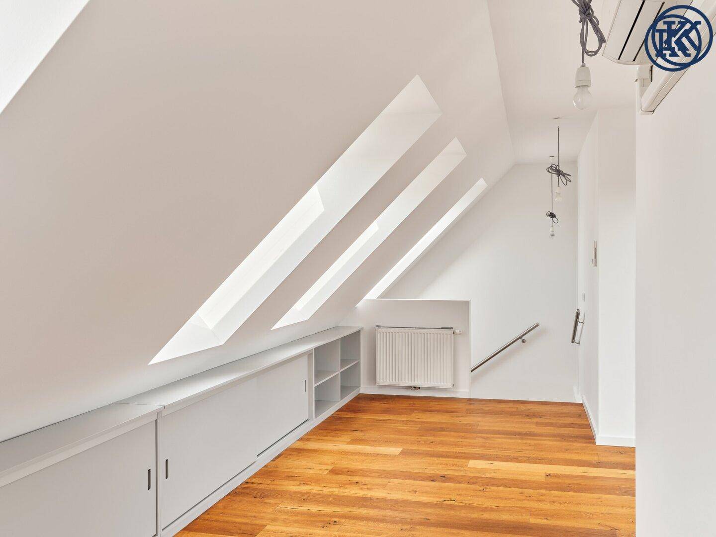 Lichtdurchflutetes Dachgeschosszimmer mit Holzboden, schrägen Wänden und integrierten Stauräumen.