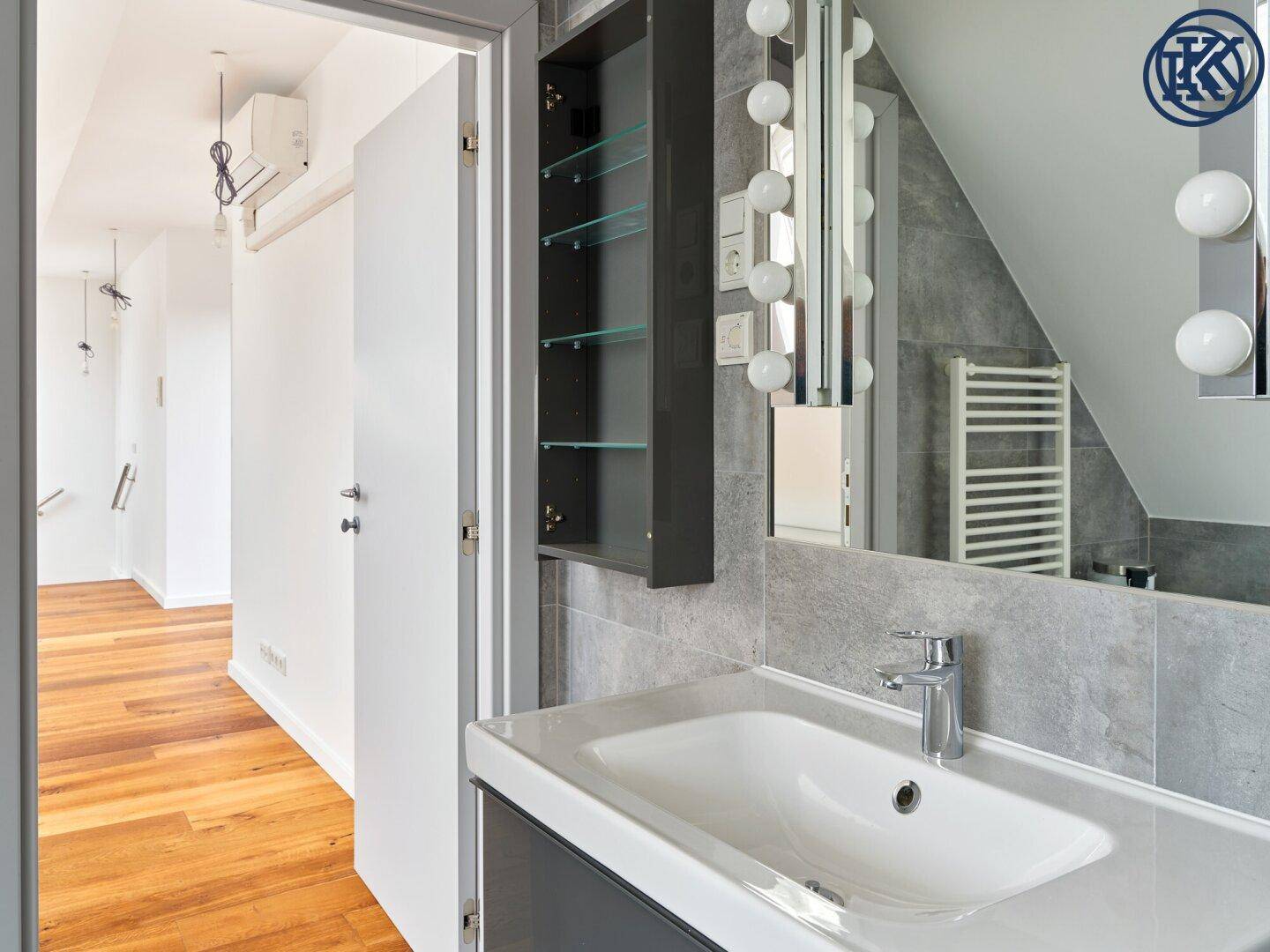 Modernes Badezimmer mit Waschtisch und Spiegelschrank, mit Blick auf den angrenzenden Flur.