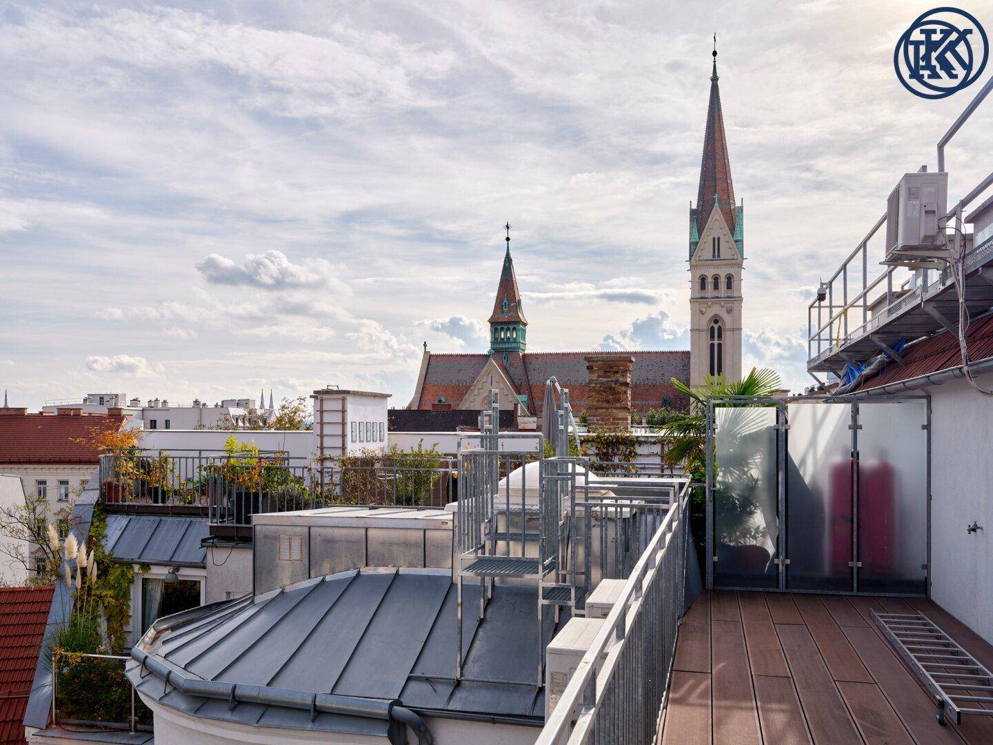 Geräumige Dachterrasse mit Holzboden und Metallgeländer, bietet einen malerischen Blick auf die Stadt und eine Kirche.