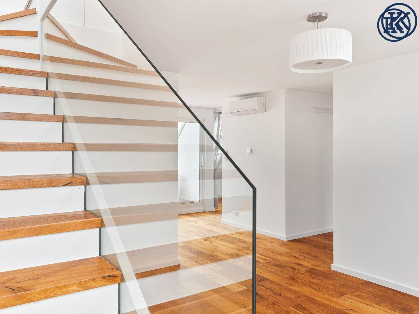 Moderner Treppenaufgang mit Holzstufen und eleganter Glasbrüstung in einem hellen Raum.