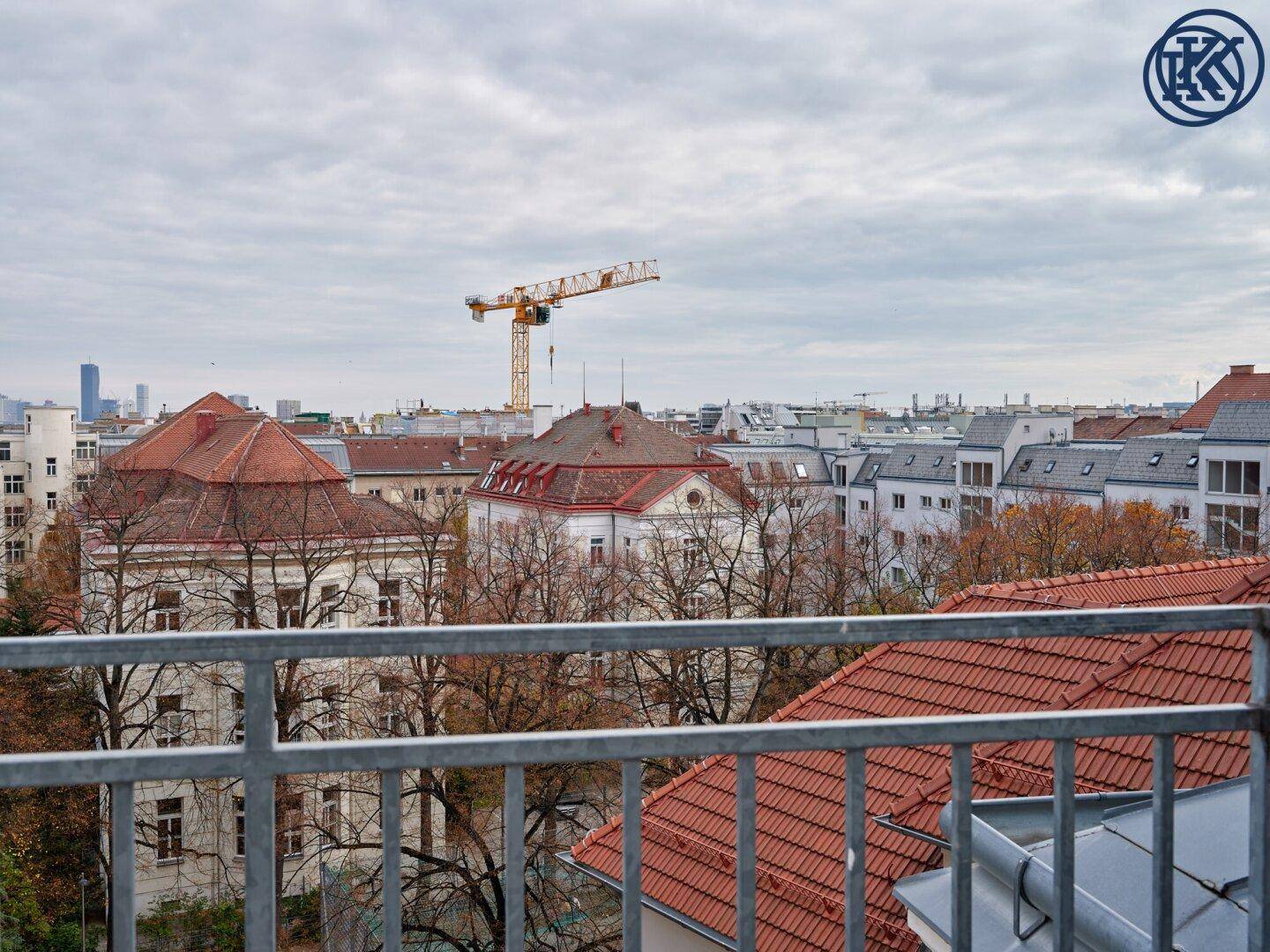 Panoramablick über die Stadt mit Dächern, Bäumen und einem Baukran am Horizont.