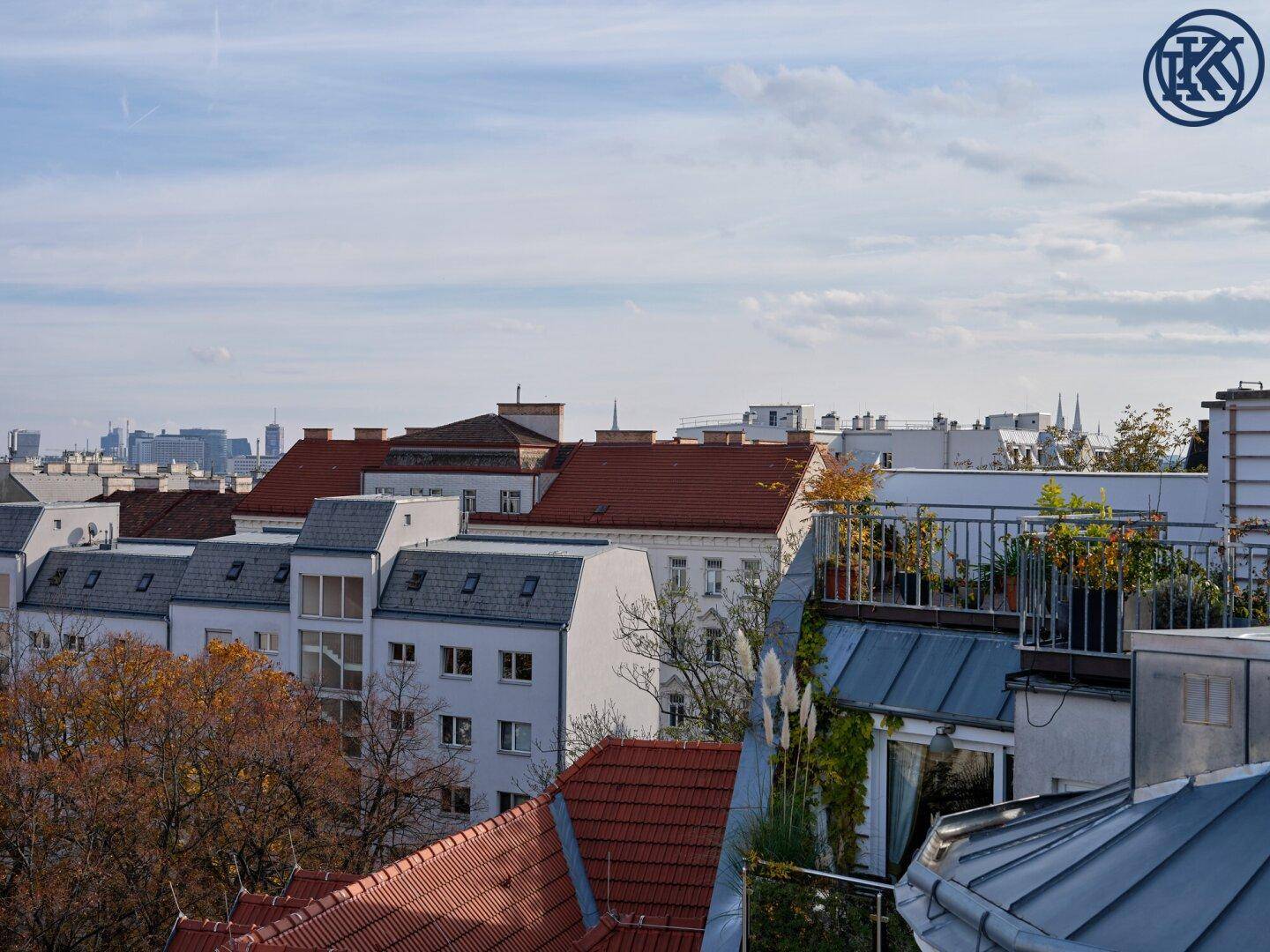 Blick über die Dächer der Stadt mit begrünten Terrassen und herbstlichen Bäumen.