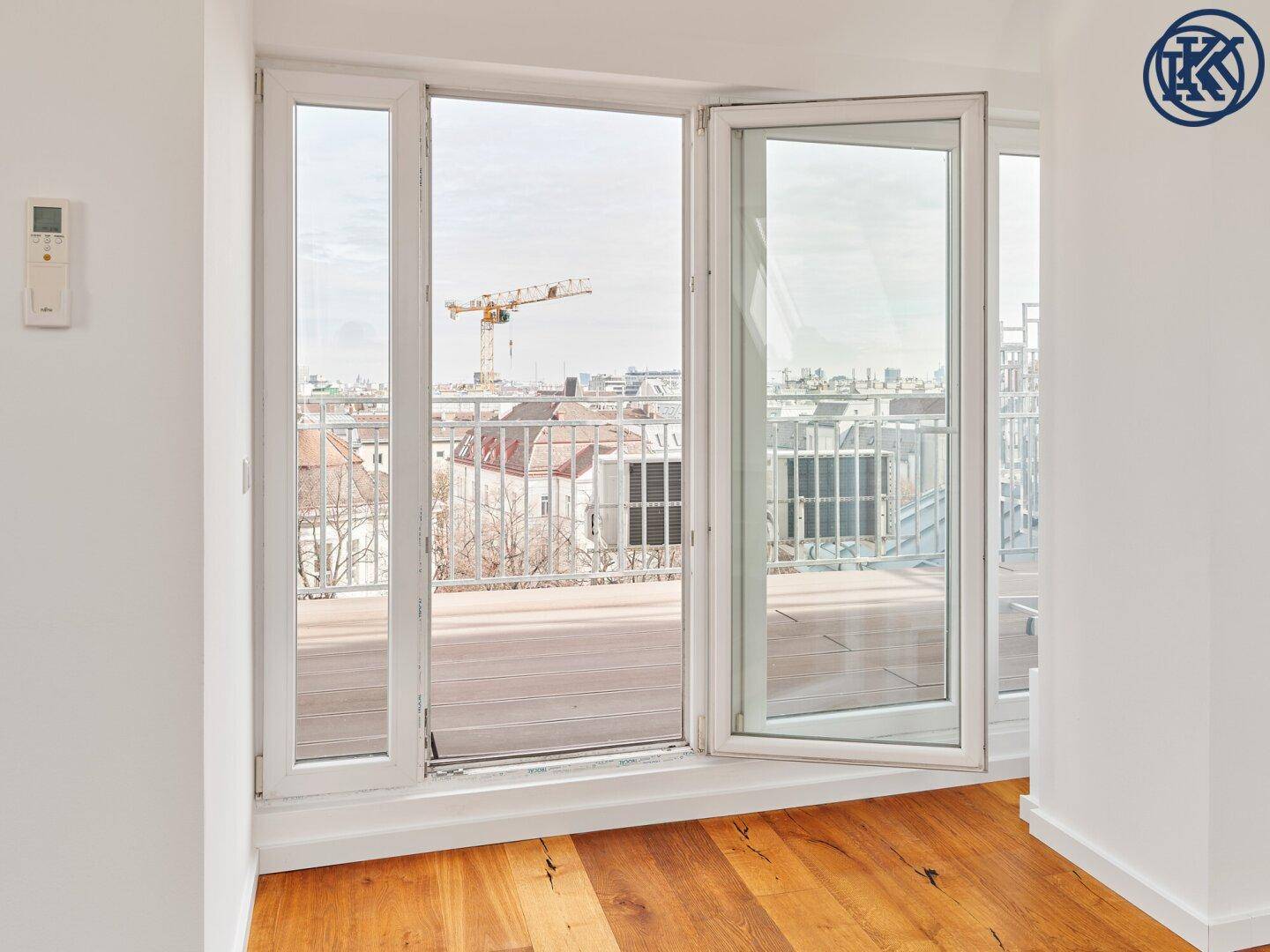 Offene Terrassentür in einem hellen Zimmer mit Holzboden und weitem Blick über die Stadt.