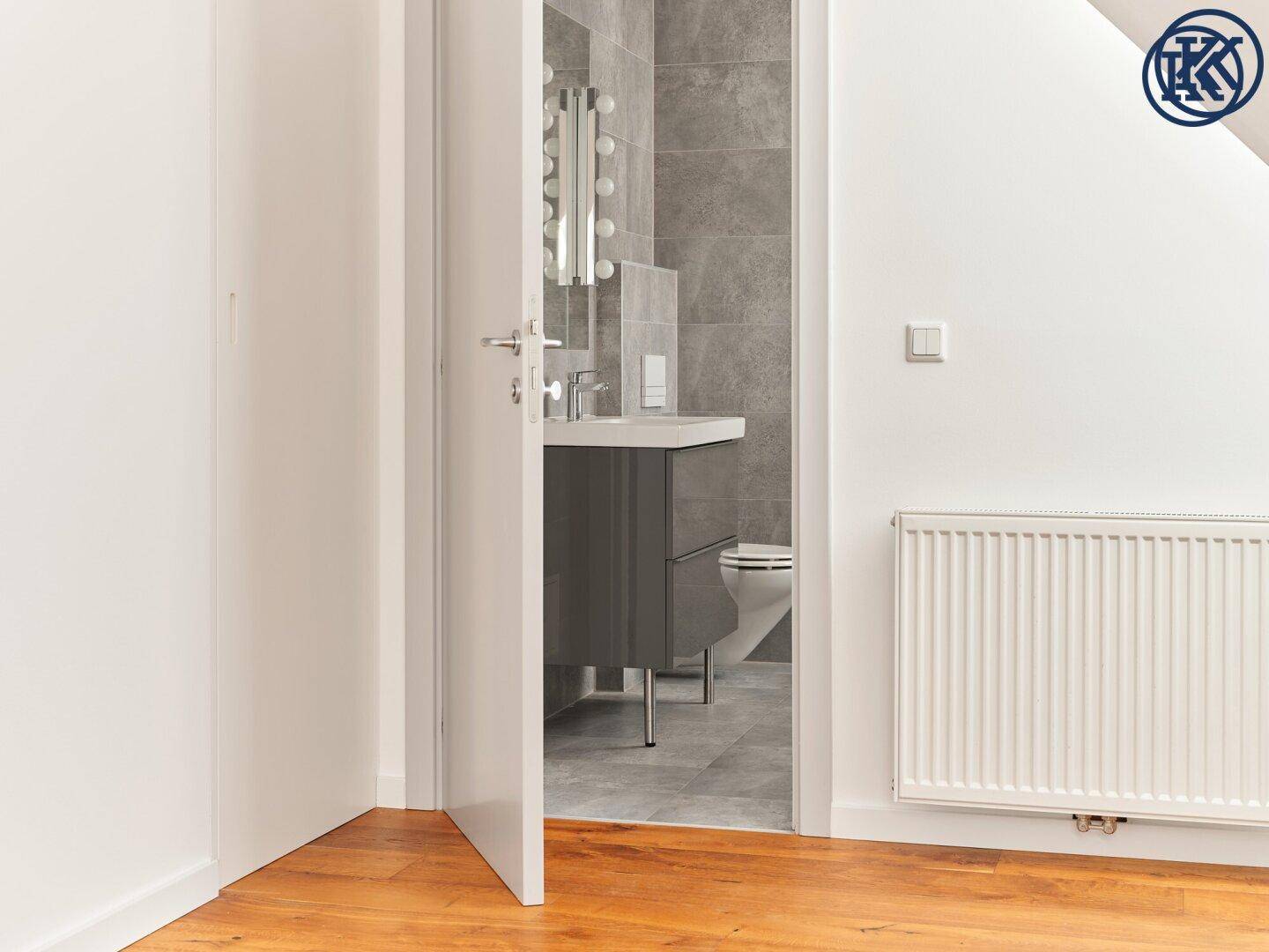 Blick durch die offene Tür auf ein modernes Badezimmer mit Waschtisch und Toilette.