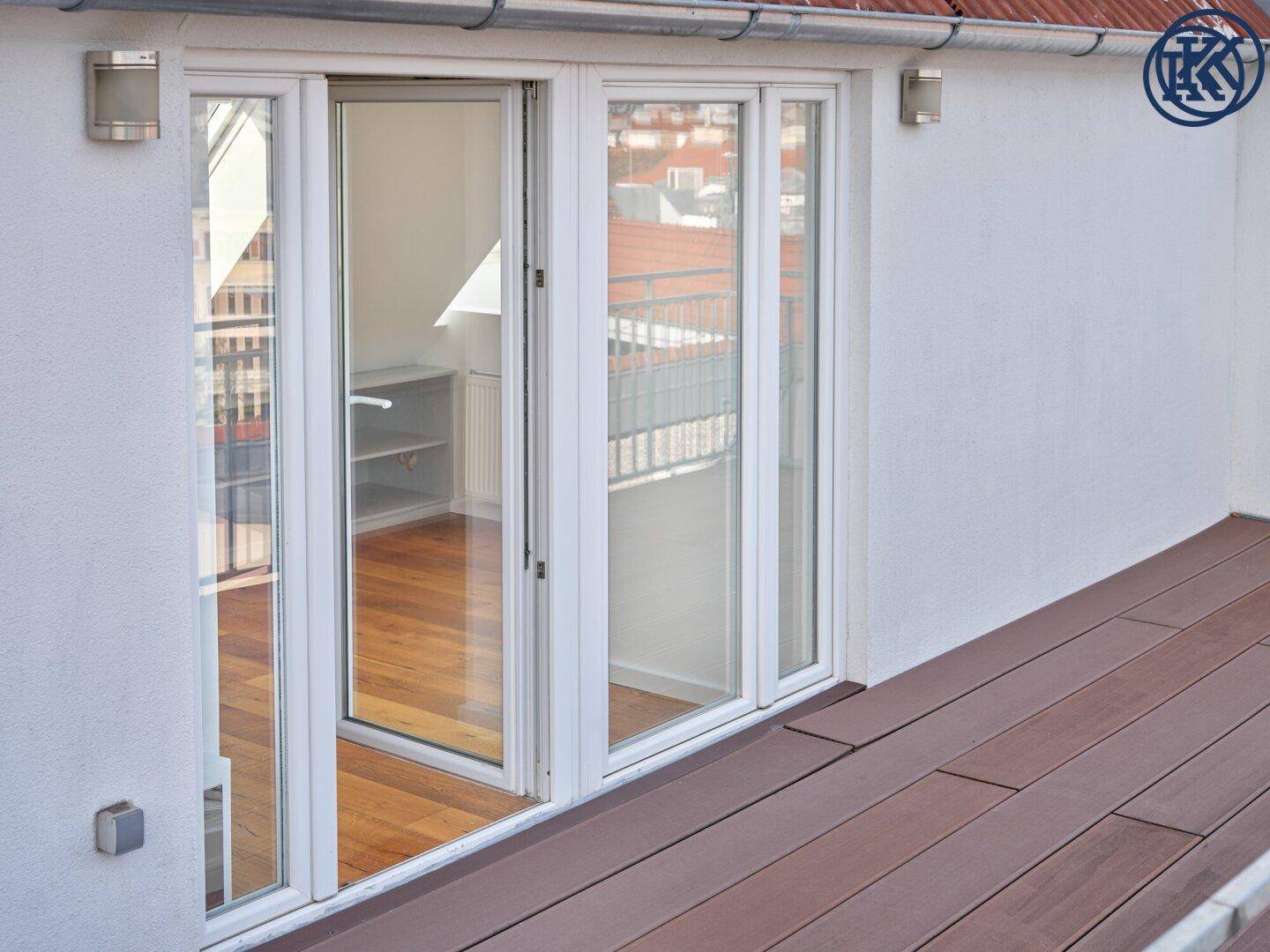 Große Glasfenster führen von einem Innenraum auf eine moderne Holzterrasse.