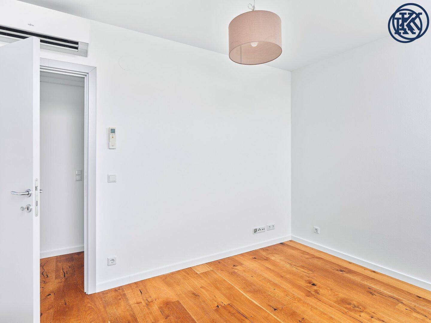 Geräumiges Schlafzimmer mit Holzboden, Klimaanlage und offenem Zugang zum Ankleidebereich.