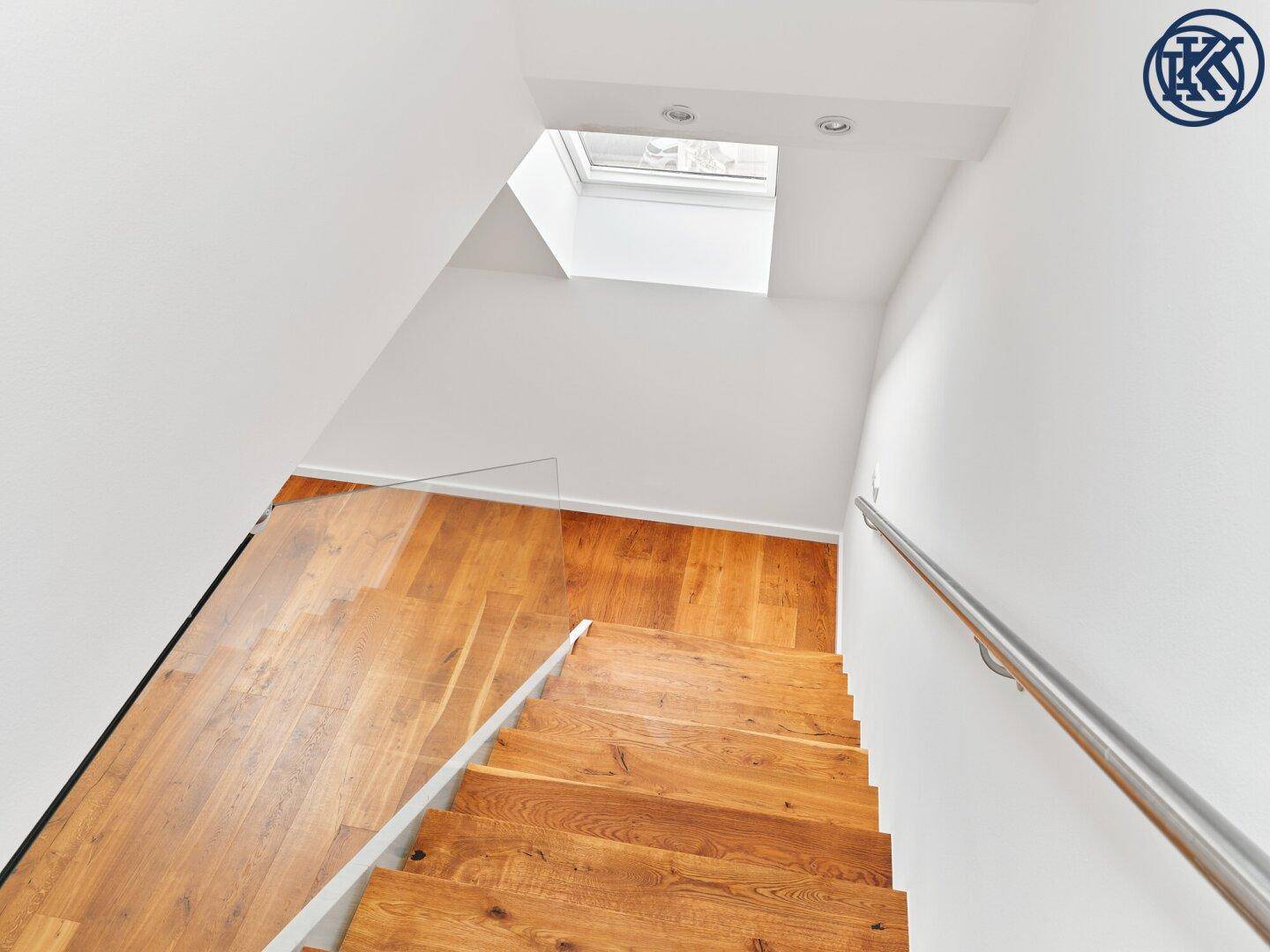 Blick von oben auf die Holztreppe mit Glasgeländer und einem Dachfenster für natürliches Licht.