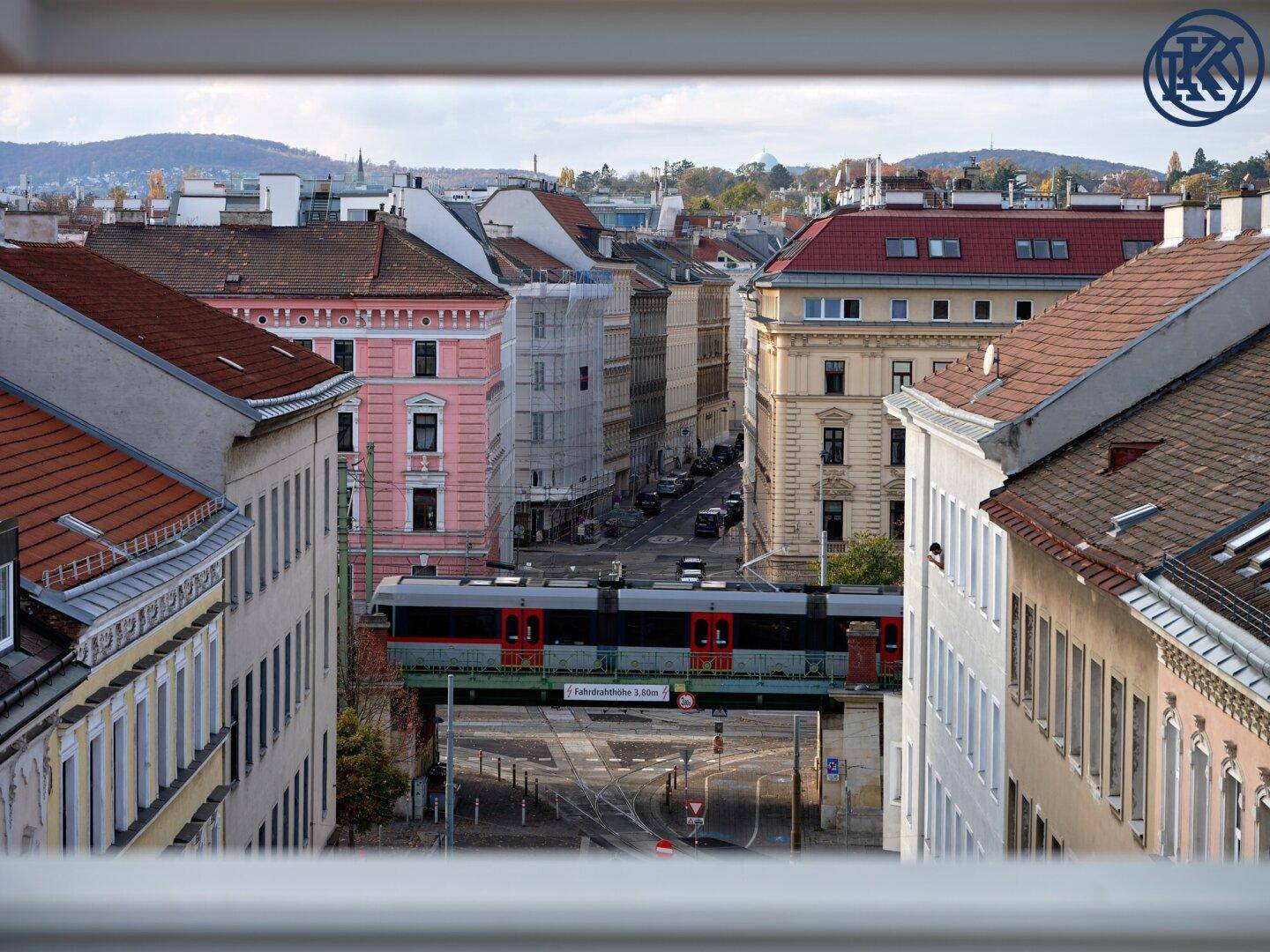 Blick aus dem Fenster auf eine belebte Stadtstraße mit historischen Gebäuden und einer Hochbahn.