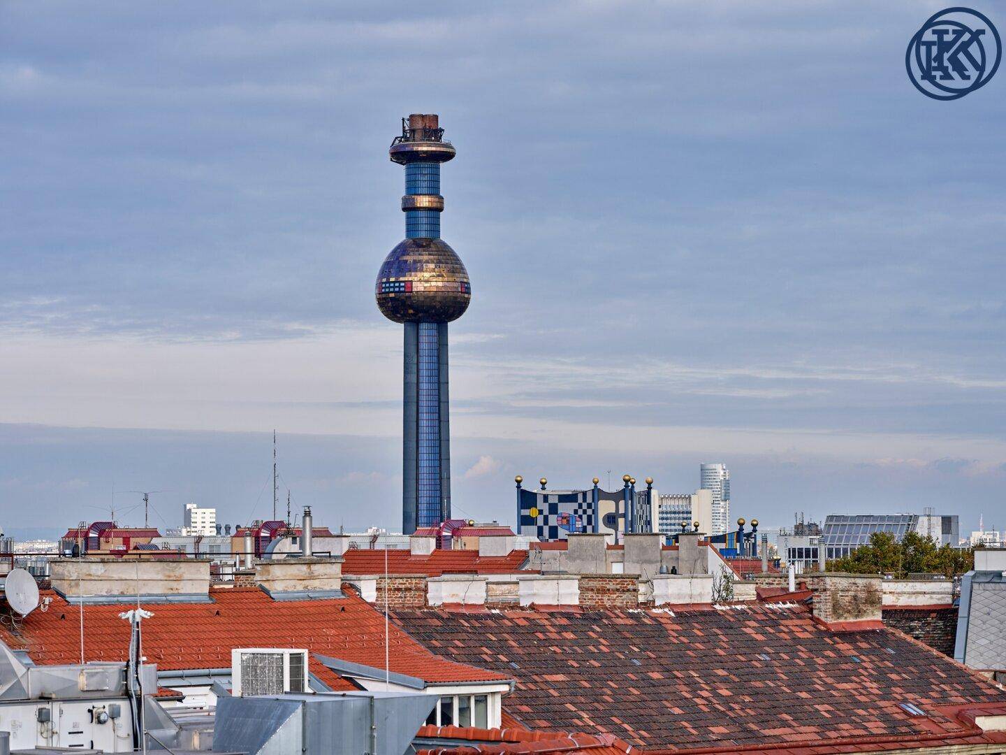 Panoramablick über die Stadt mit dem markanten Fernwärmeturm Spittelau unter bewölktem Himmel.