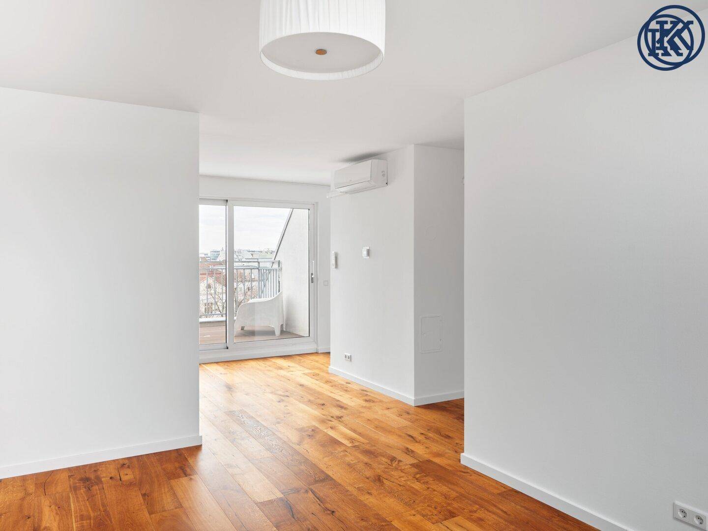 Heller Wohnbereich mit Holzboden, Klimaanlage und großem Schiebefenster zum Balkon.
