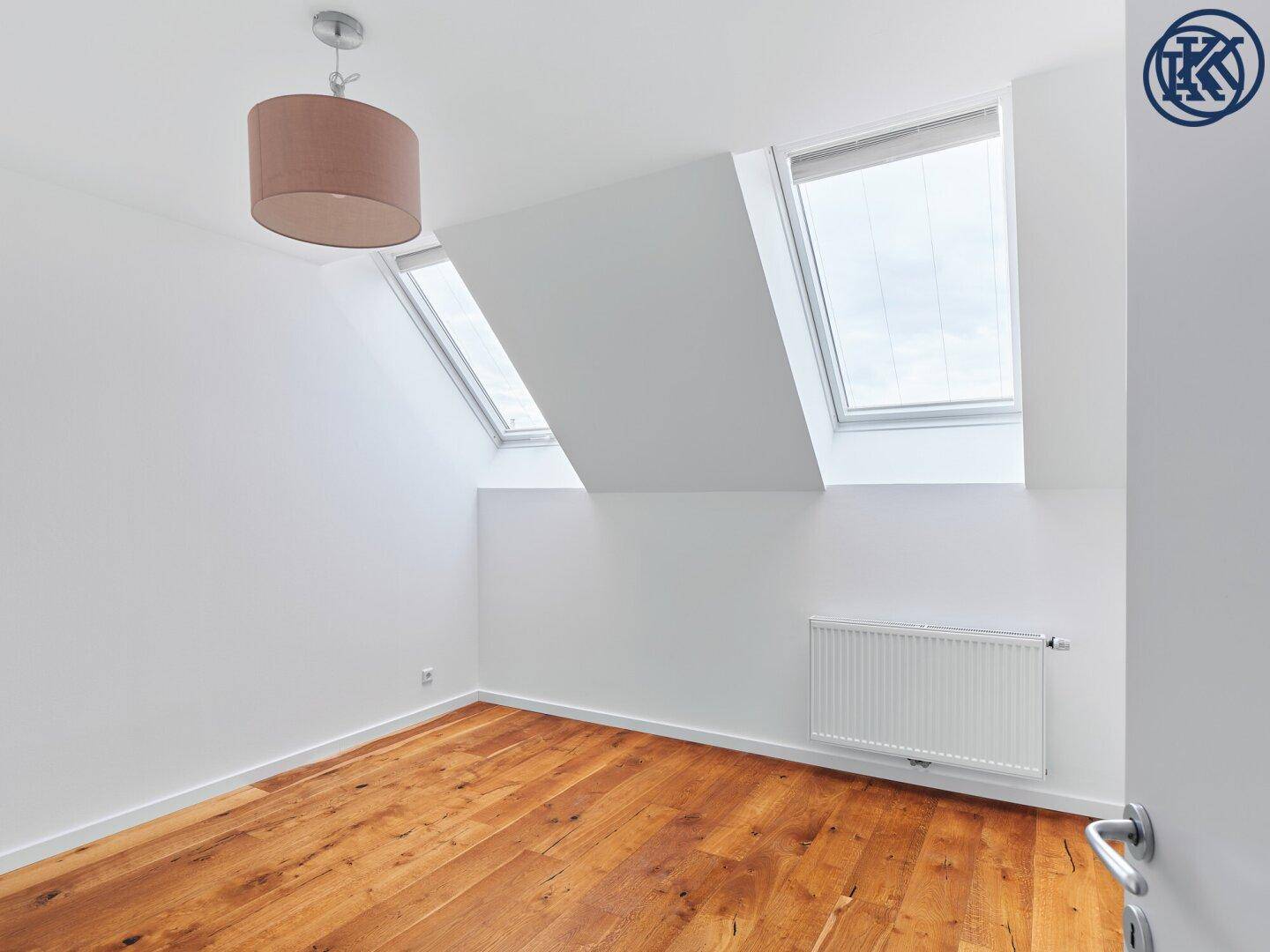 Helles Schlafzimmer im Dachgeschoss mit Holzboden, schrägen Wänden und zwei großen Dachfenstern.