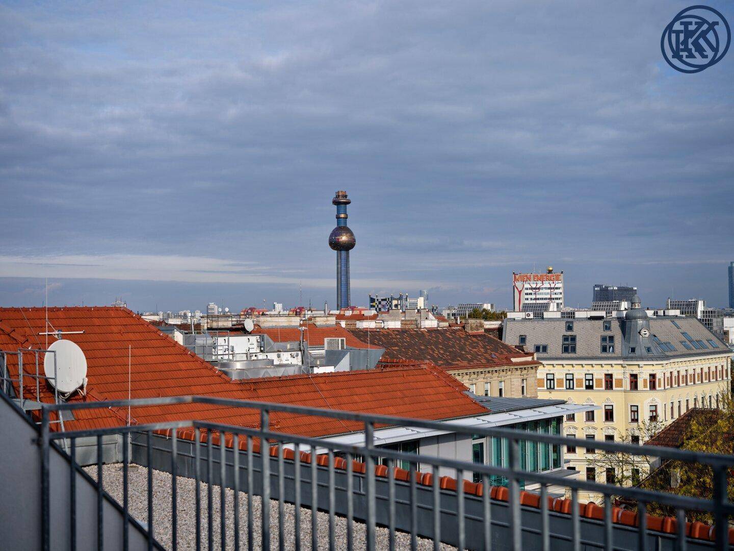 Weitläufiger Blick über die Dächer der Stadt mit dem Fernwärmeturm Spittelau im Hintergrund.