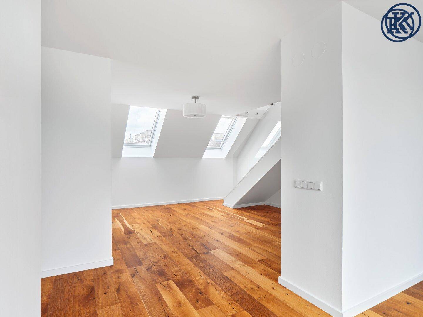Heller Dachgeschossraum mit Holzboden und mehreren Dachfenstern, der viel Tageslicht hereinlässt.