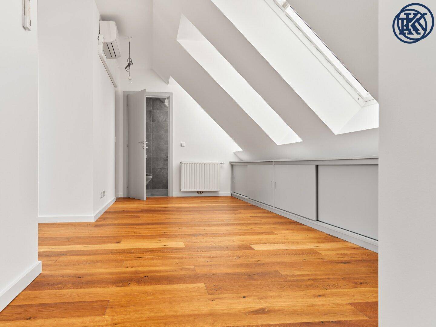 Geräumiges Dachzimmer mit Holzboden, Einbauschränken und mehreren Dachfenstern für viel Licht.