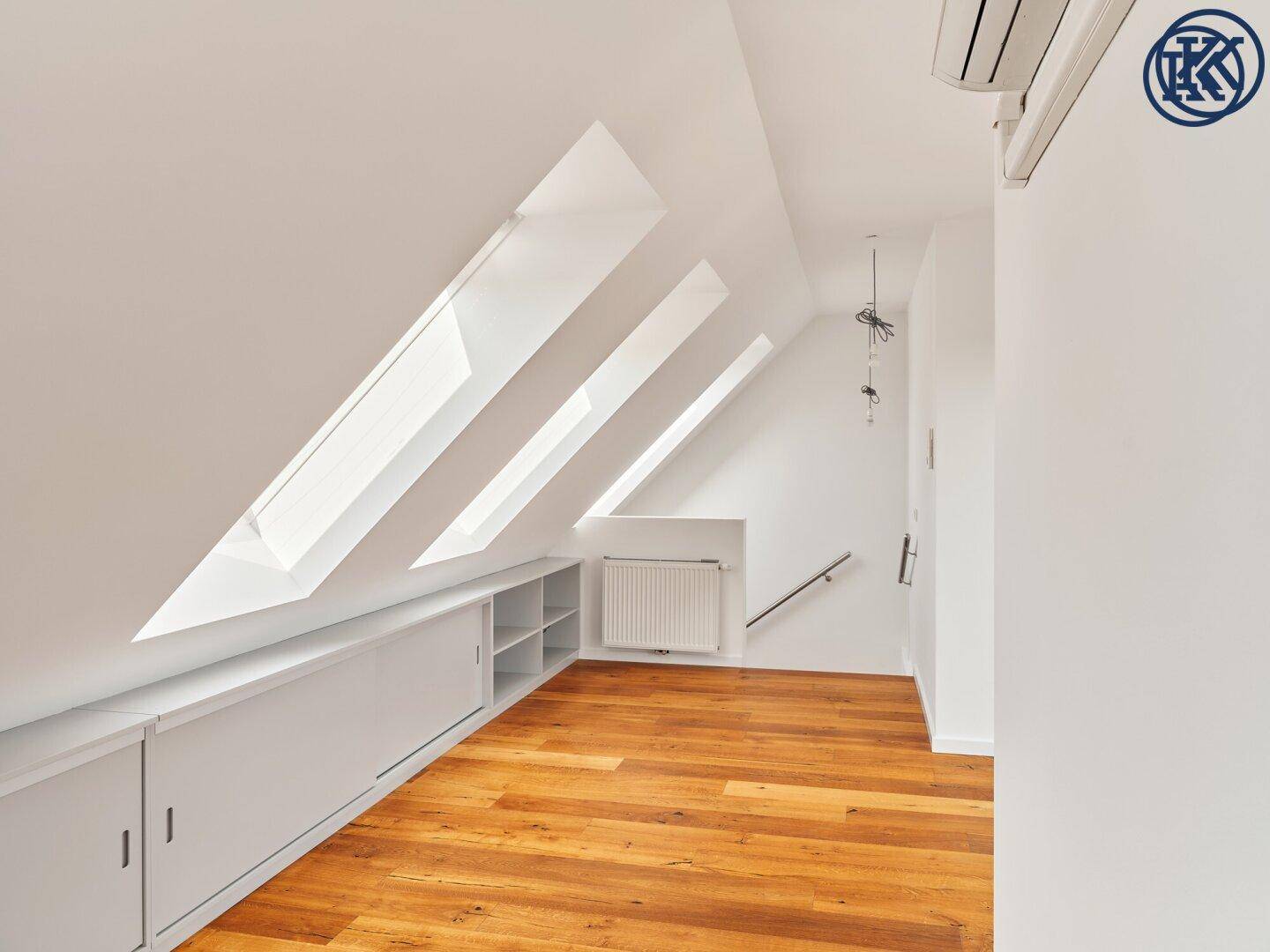 Geräumiges Dachzimmer mit Holzboden, Einbauschränken und mehreren schrägen Dachfenstern.