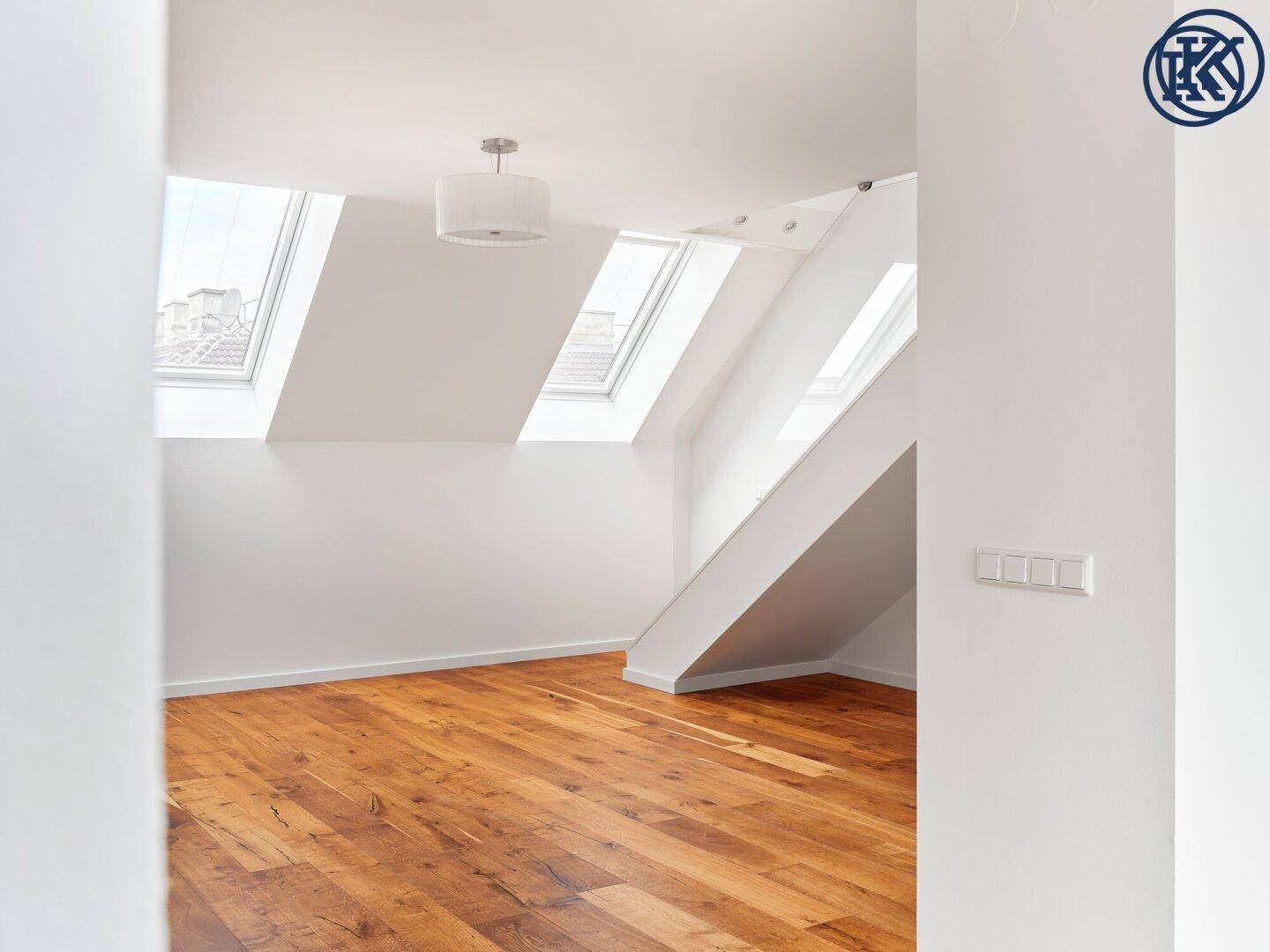 Heller Dachgeschossraum mit Holzboden und mehreren Dachfenstern, der viel Tageslicht hereinlässt.