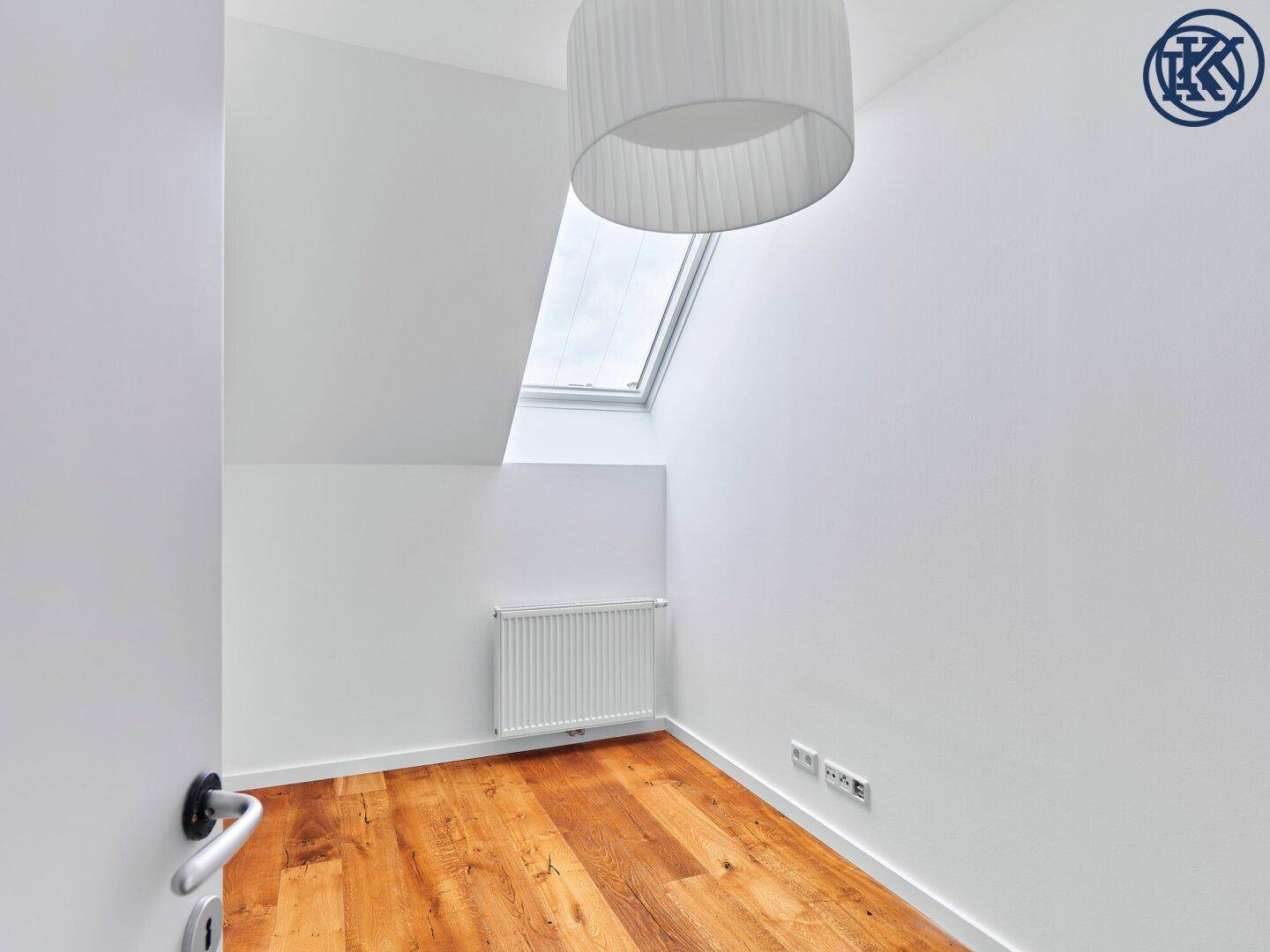 Kleines, helles Schlafzimmer im Dachgeschoss mit Holzboden, Heizkörper und einem Dachfenster.