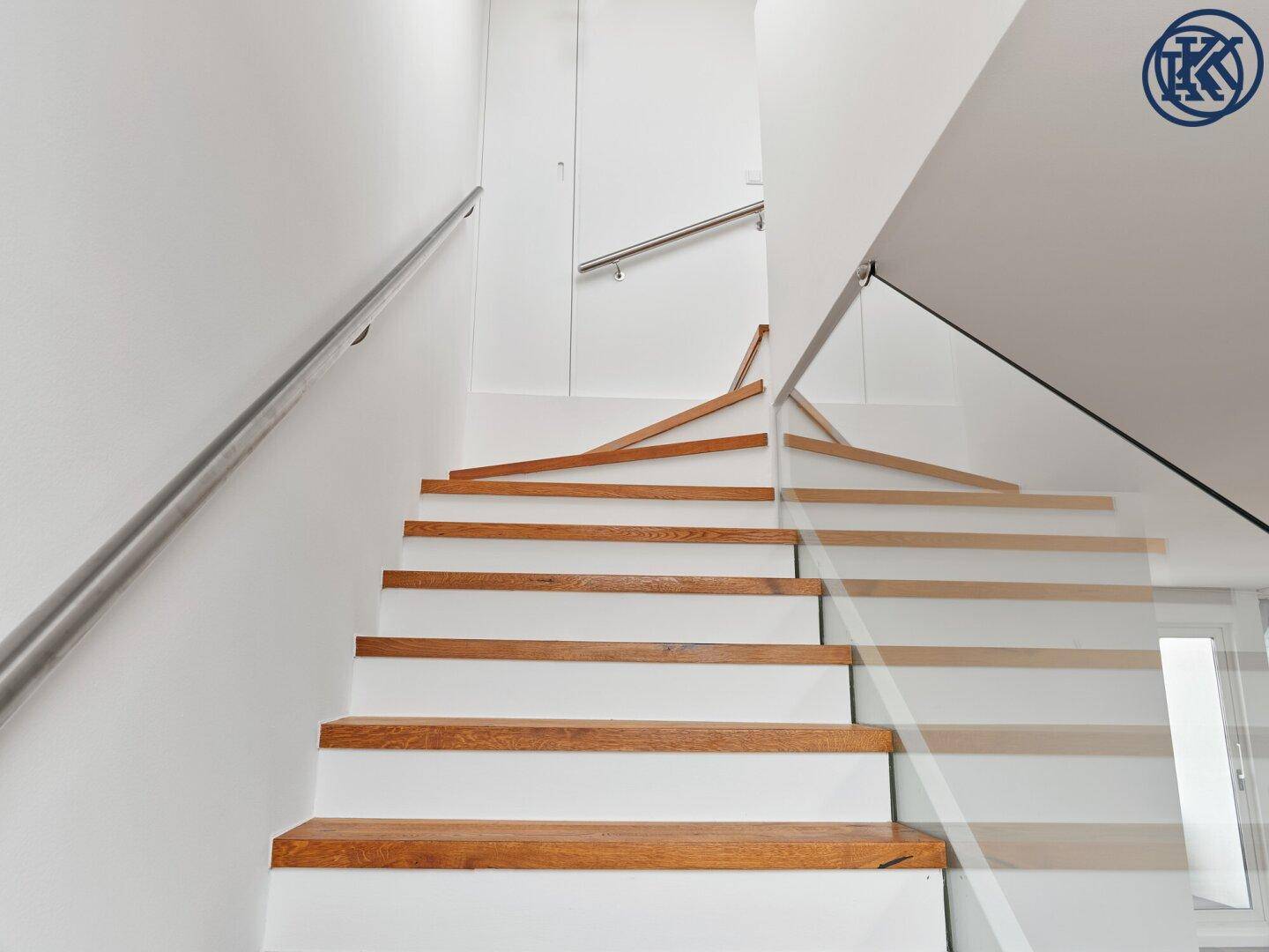 Moderne Holztreppe mit Glasgeländer und Edelstahlhandlauf, die zu den oberen Etagen führt.