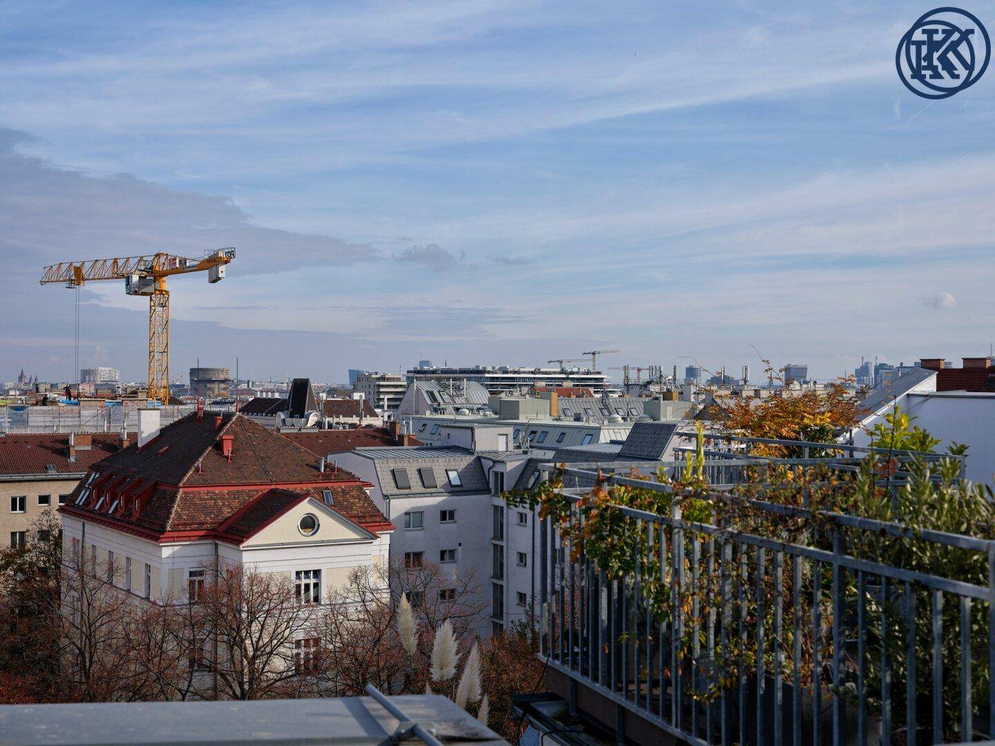 Panoramablick von einer Terrasse über die Stadt mit einem Baukran und herbstlichen Bäumen.
