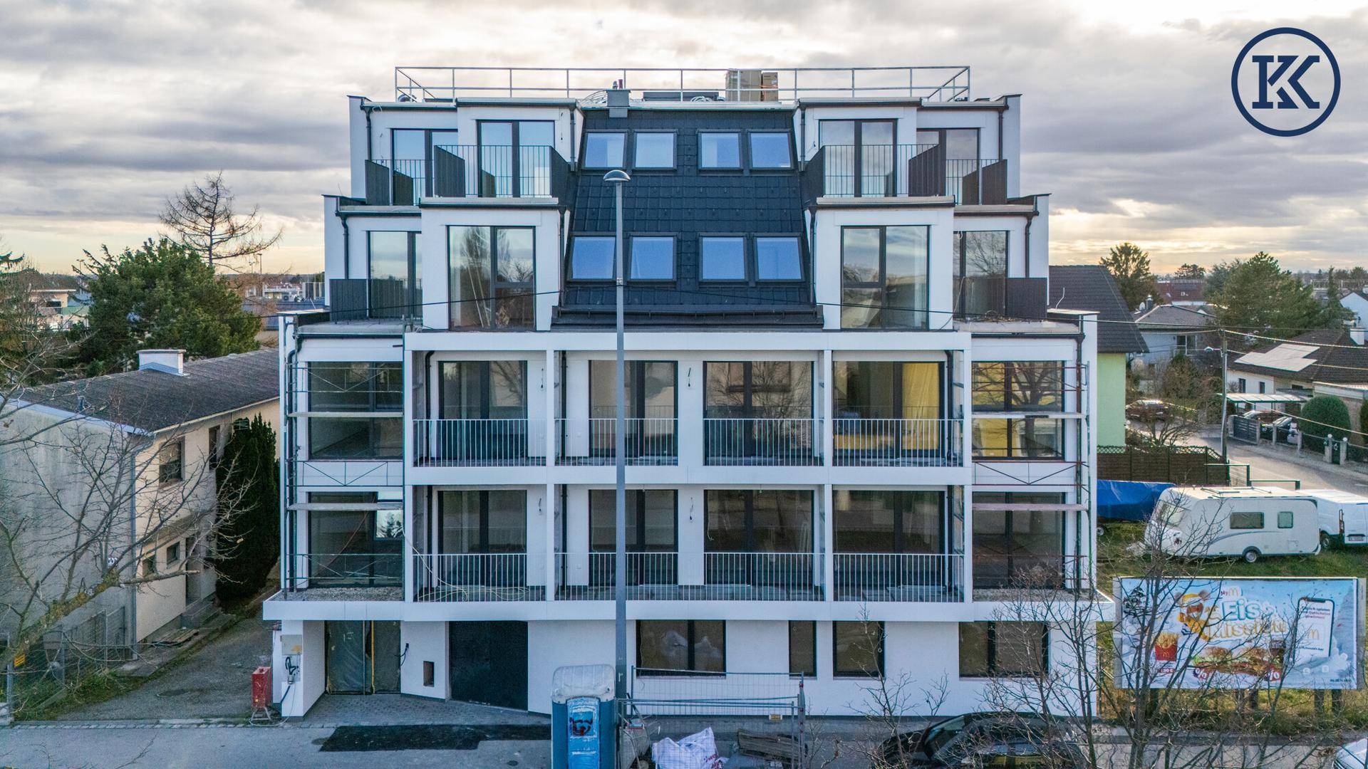 Modernes Mehrfamilienhaus mit mehreren Balkonen und großen Fenstern in einer städtischen Umgebung.