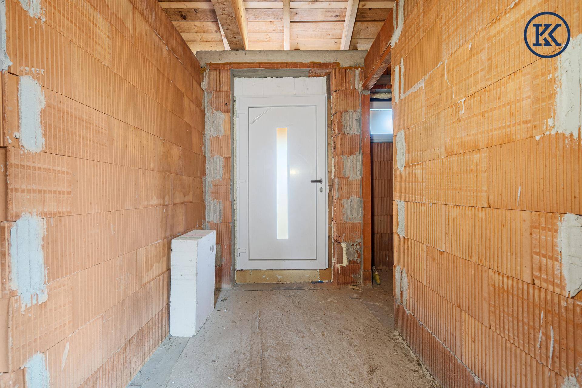 Eingangsbereich im Rohbau mit einer weißen Tür und unverputzten Ziegelwänden.