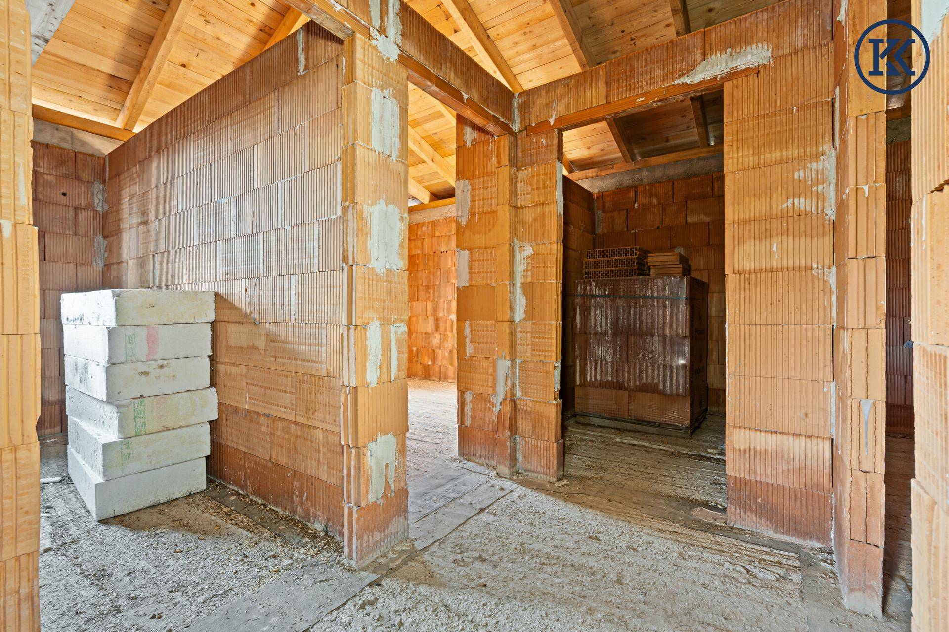 Rohbau-Innenraum mit gestapelten Baumaterialien und sichtbarer Holzdecke, bereit für den Ausbau.