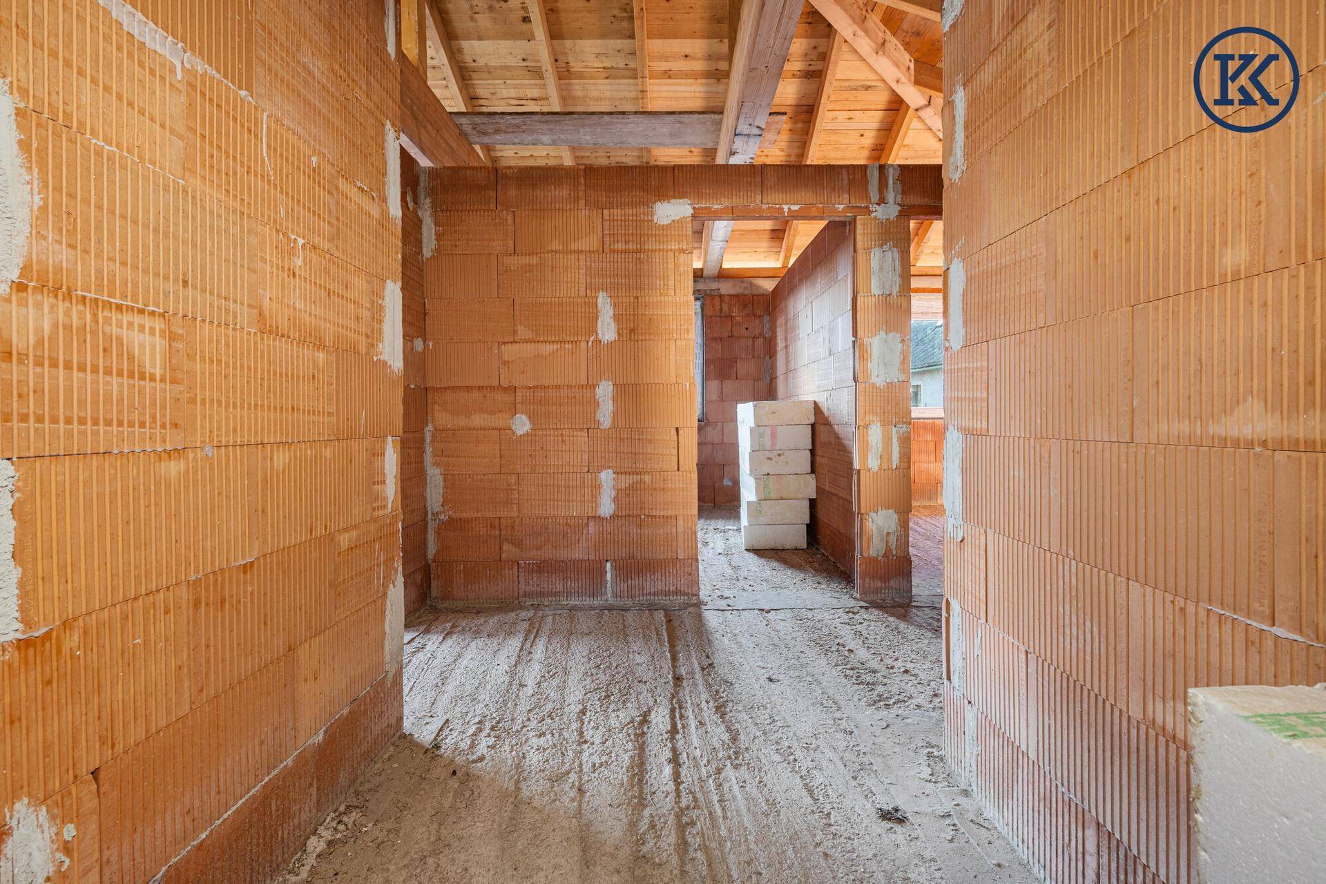 Innenansicht eines Rohbaus mit Ziegelwänden und sichtbarer Holzdecke, bereit für den Ausbau.