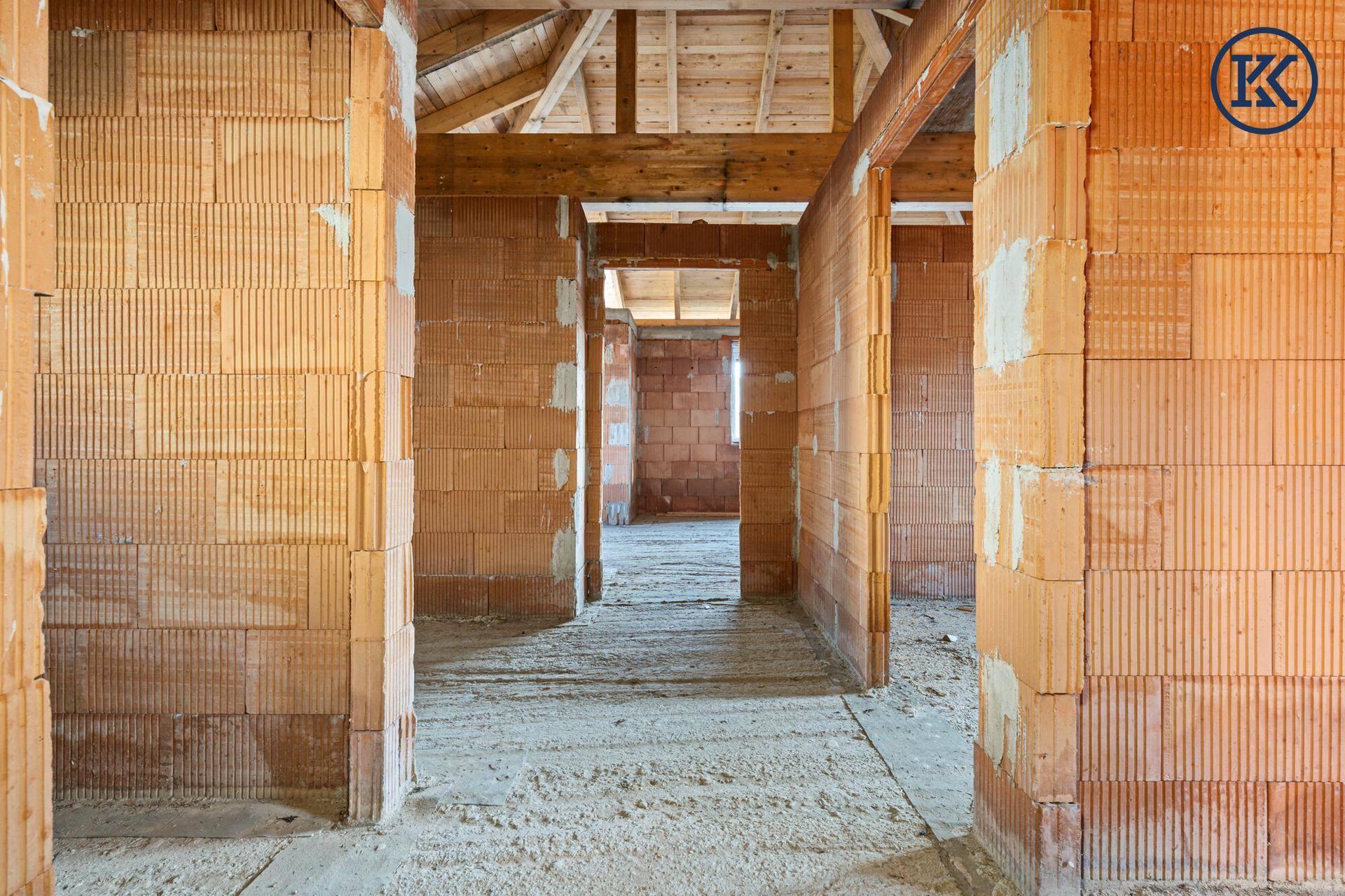 Rohbau-Innenraum mit Ziegelwänden und offener Holzkonstruktion des Daches, viel Tageslicht.