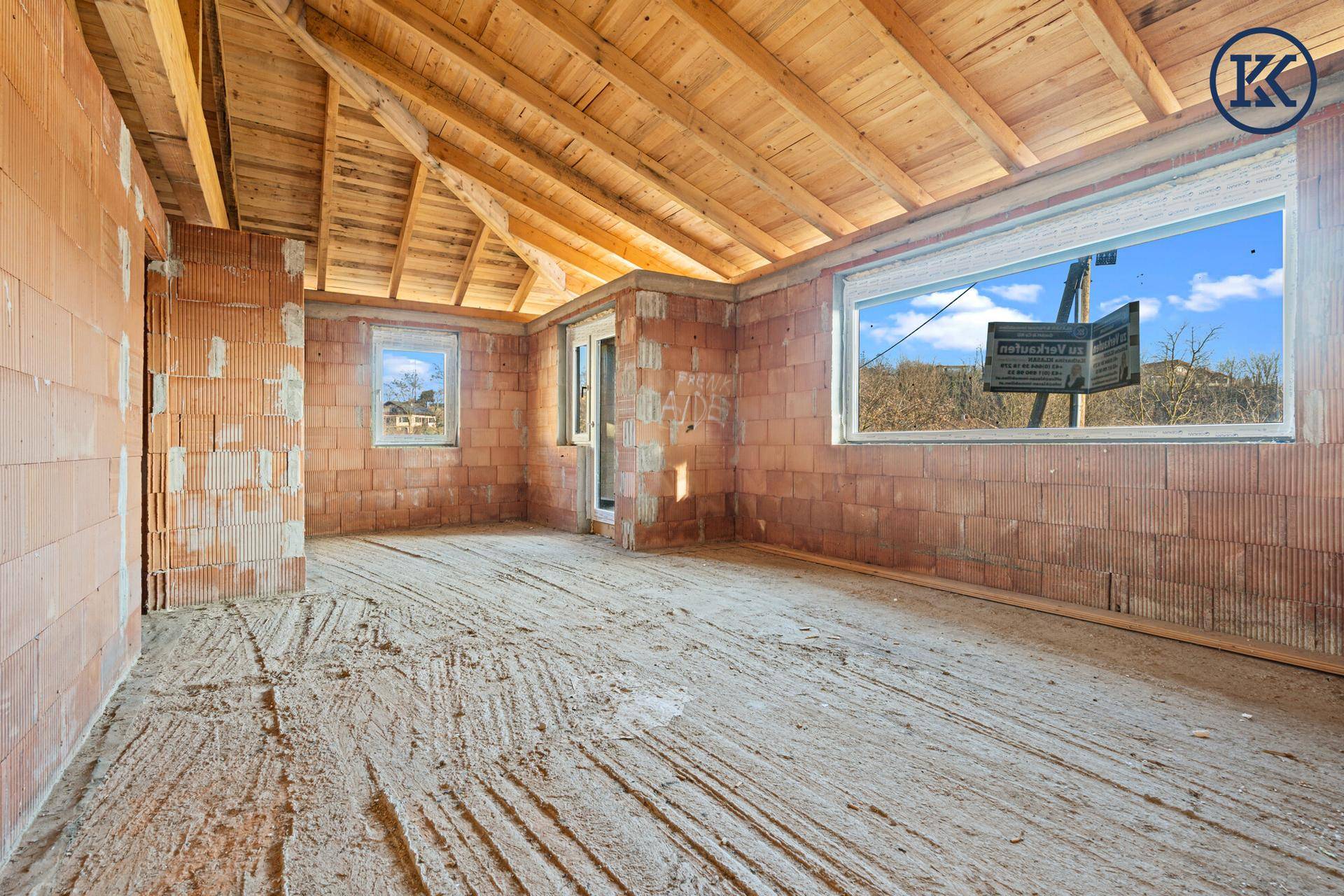 Geräumiger Rohbau-Innenraum mit Ziegelwänden, Holzdecke und weitem Blick durch die Fenster.