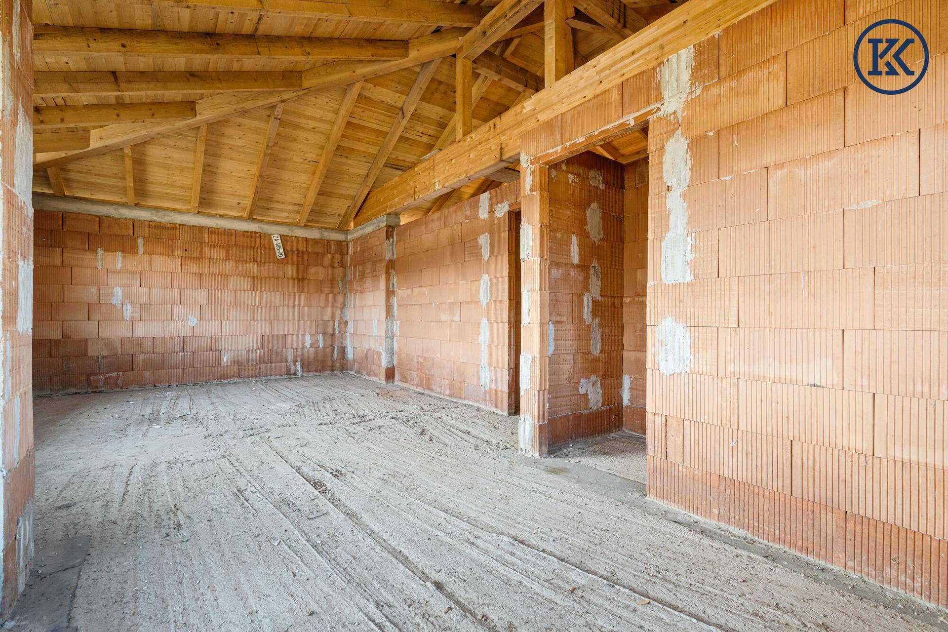 Großer Rohbau-Raum mit Ziegelwänden und sichtbarer Holzdecke, bereit für den Innenausbau.
