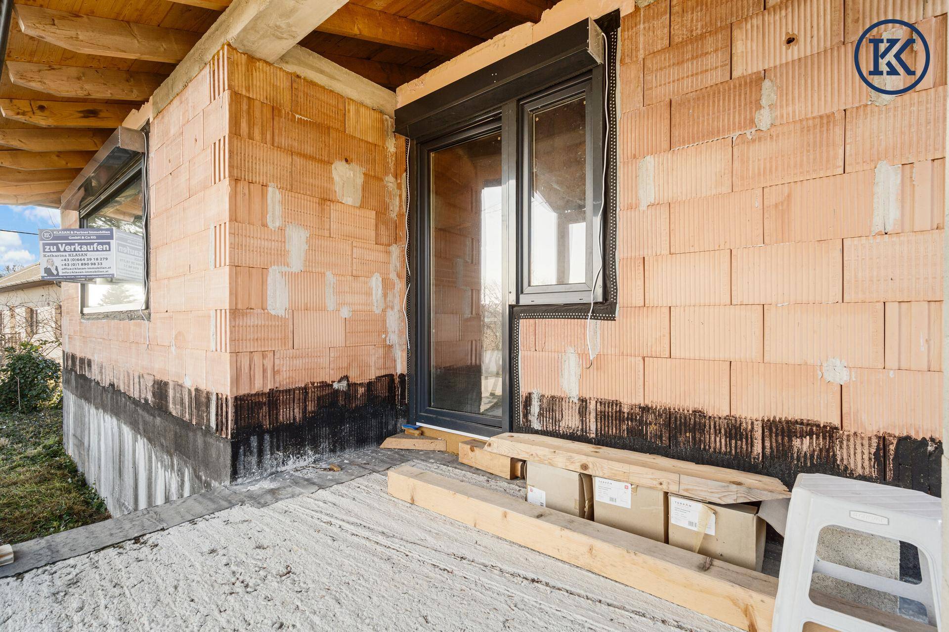 Überdachter Bereich am Rohbau mit Ziegelwänden und einem Fenster mit Rollladen.