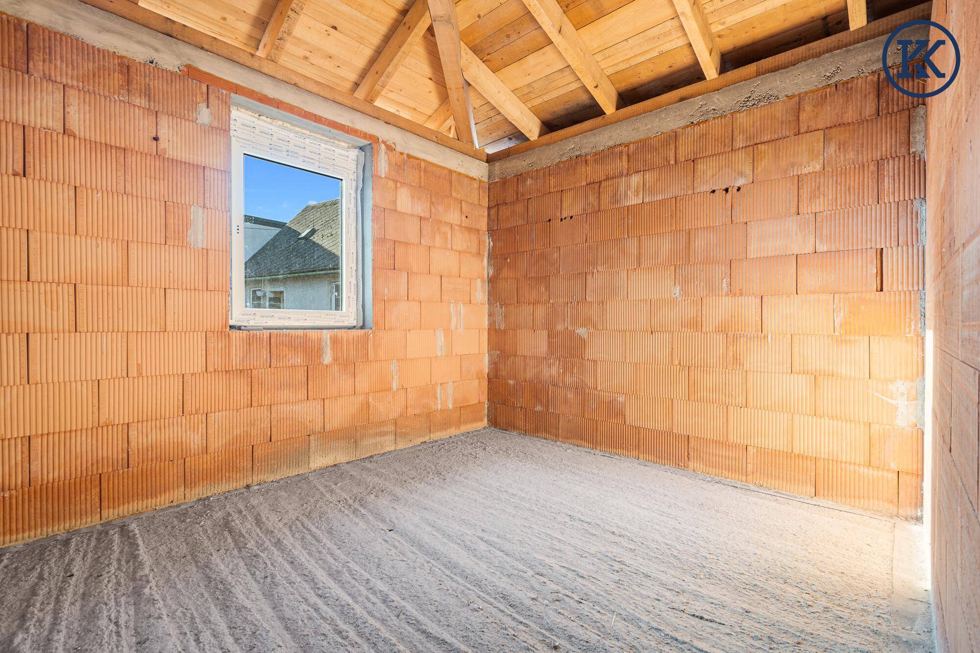 Kleiner Raum im Rohbau mit Ziegelwänden und einem Fenster, das den Blick nach draußen freigibt.
