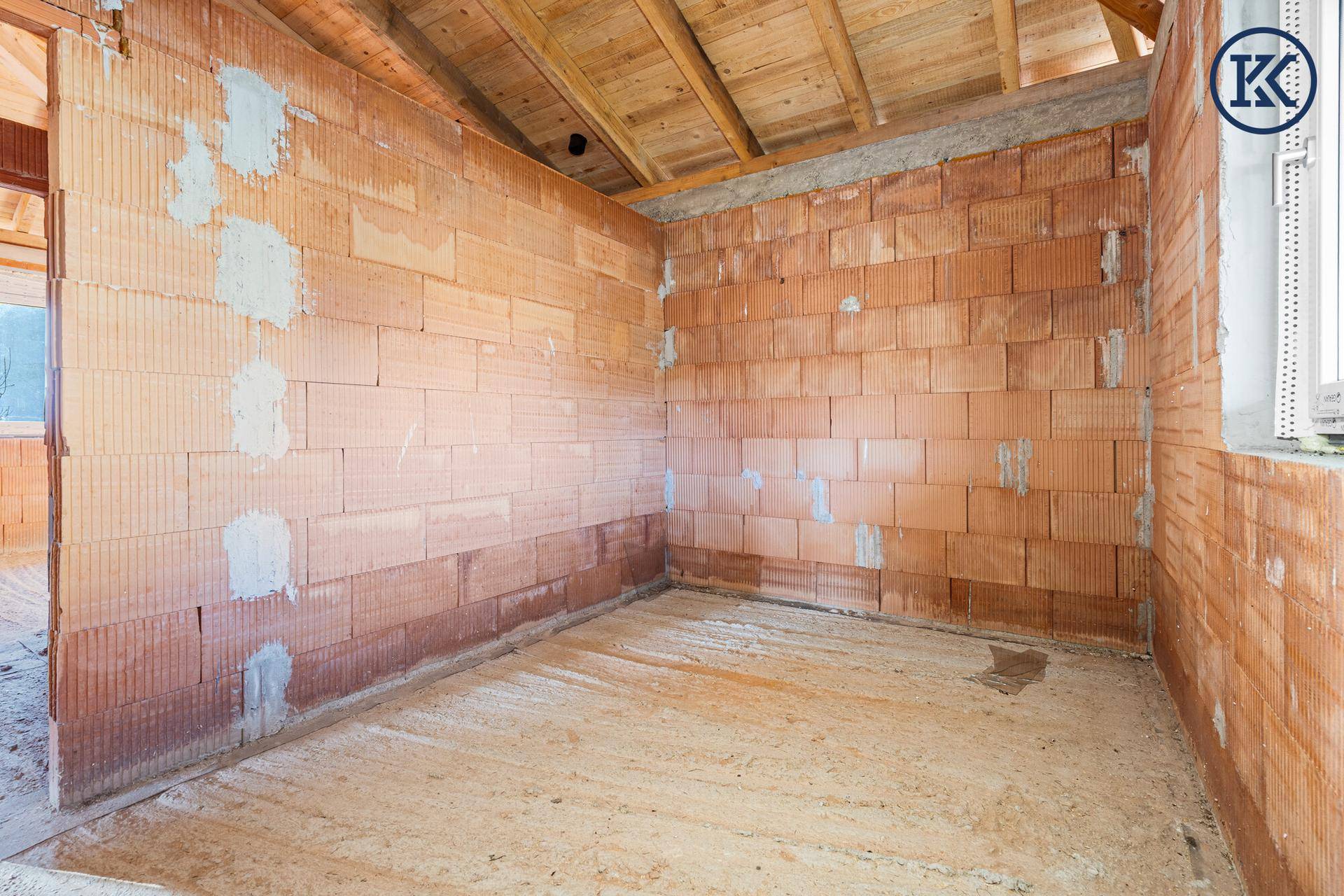 Rohbau-Raum mit Ziegelwänden und sichtbarer Holzdecke, bereit für den Innenausbau.
