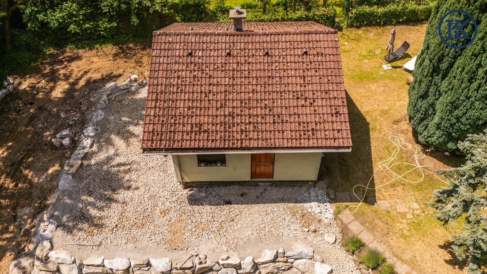 Luftaufnahme eines Hauses mit Ziegeldach, Kiesfläche und umgebendem Grün.