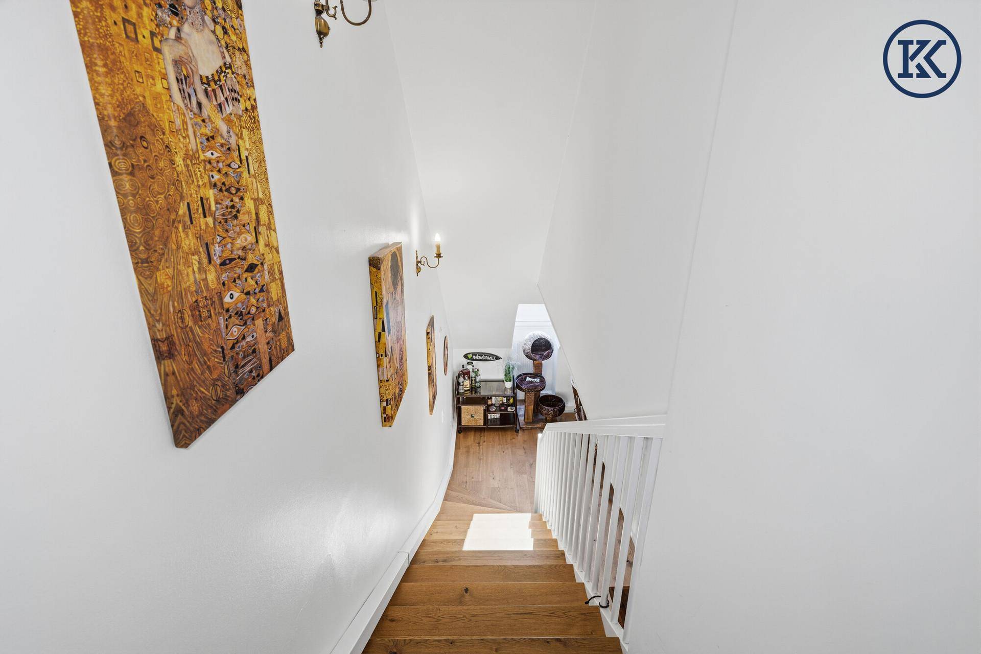 Helle Treppe mit weißem Geländer und Kunstwerken an der Wand, die in den unteren Bereich führt.