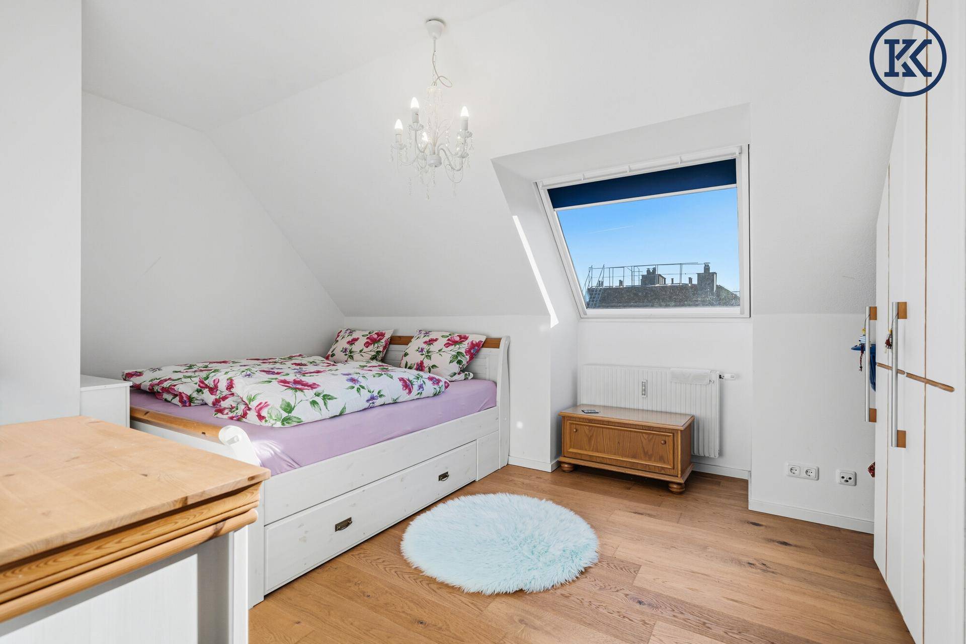 Helles Schlafzimmer mit Holzboden, Bett mit Stauraum und Dachfenster unter der Schräge.