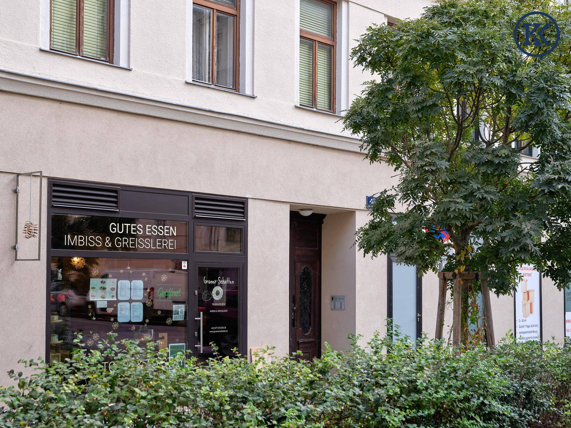 Erdgeschoss eines Gebäudes mit einem Geschäft und einem Baum vor der Fassade.
