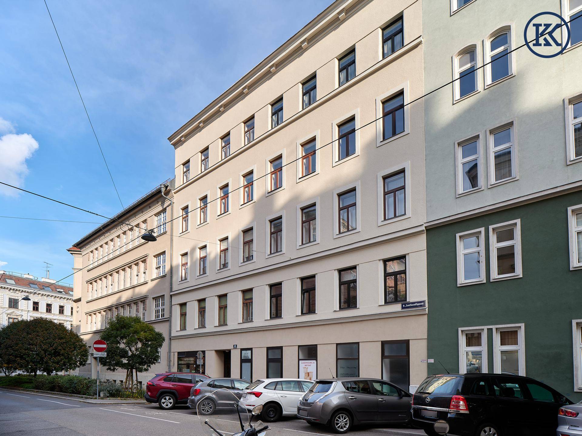 Mehrstöckiges Wohngebäude mit klassischer Fassade und parkenden Autos auf der Straße.