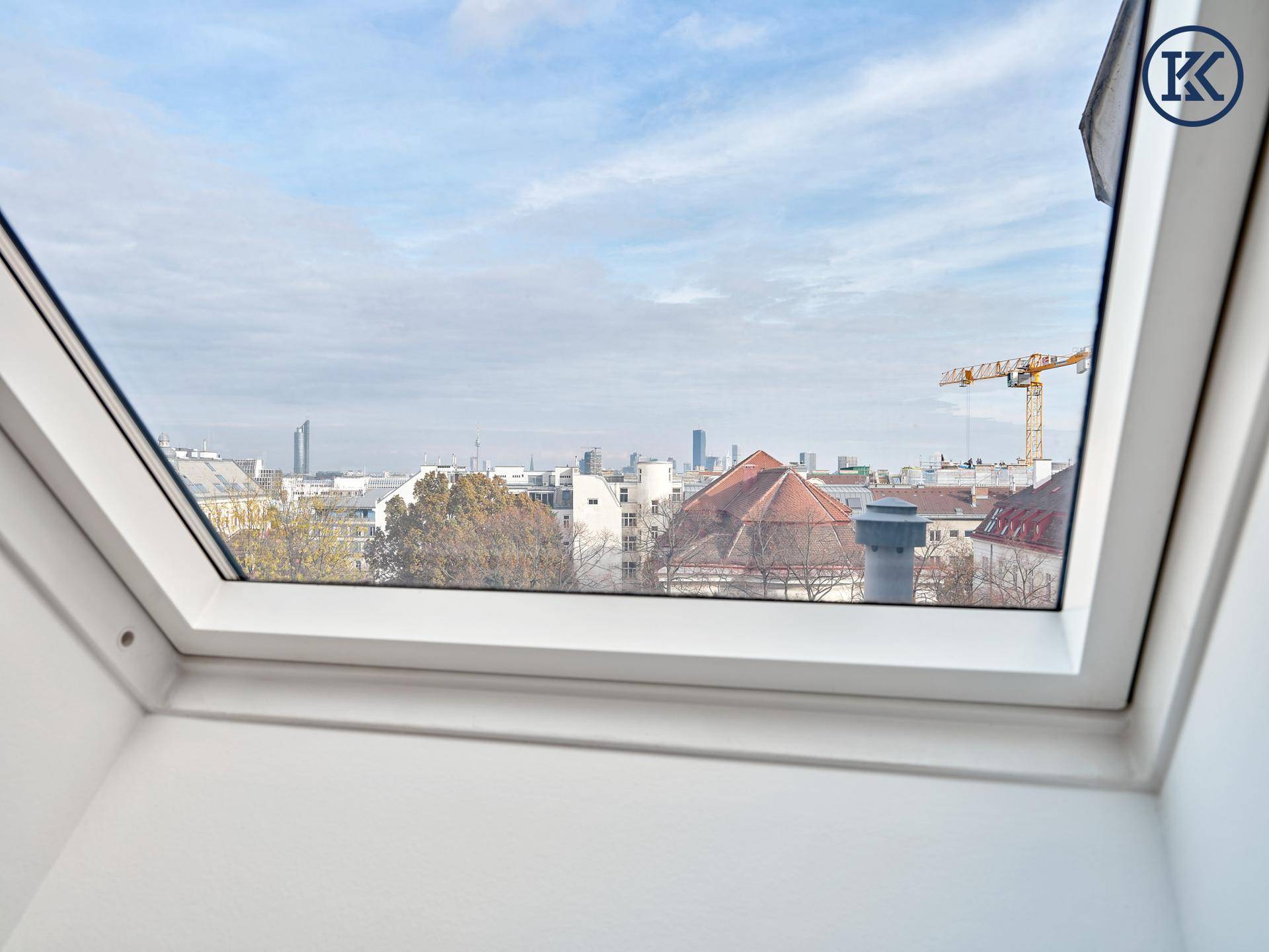 Weitblick über die Stadt aus einem Dachfenster mit urbaner Skyline im Hintergrund.