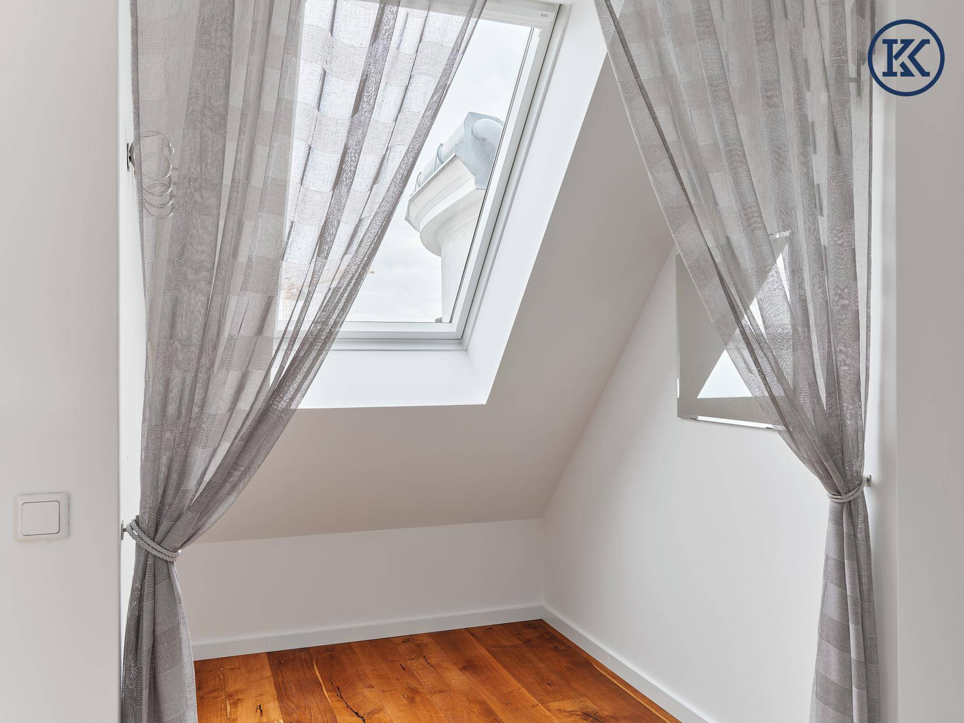 Heller Dachgeschossbereich mit Holzboden, Dachfenster und Vorhängen.